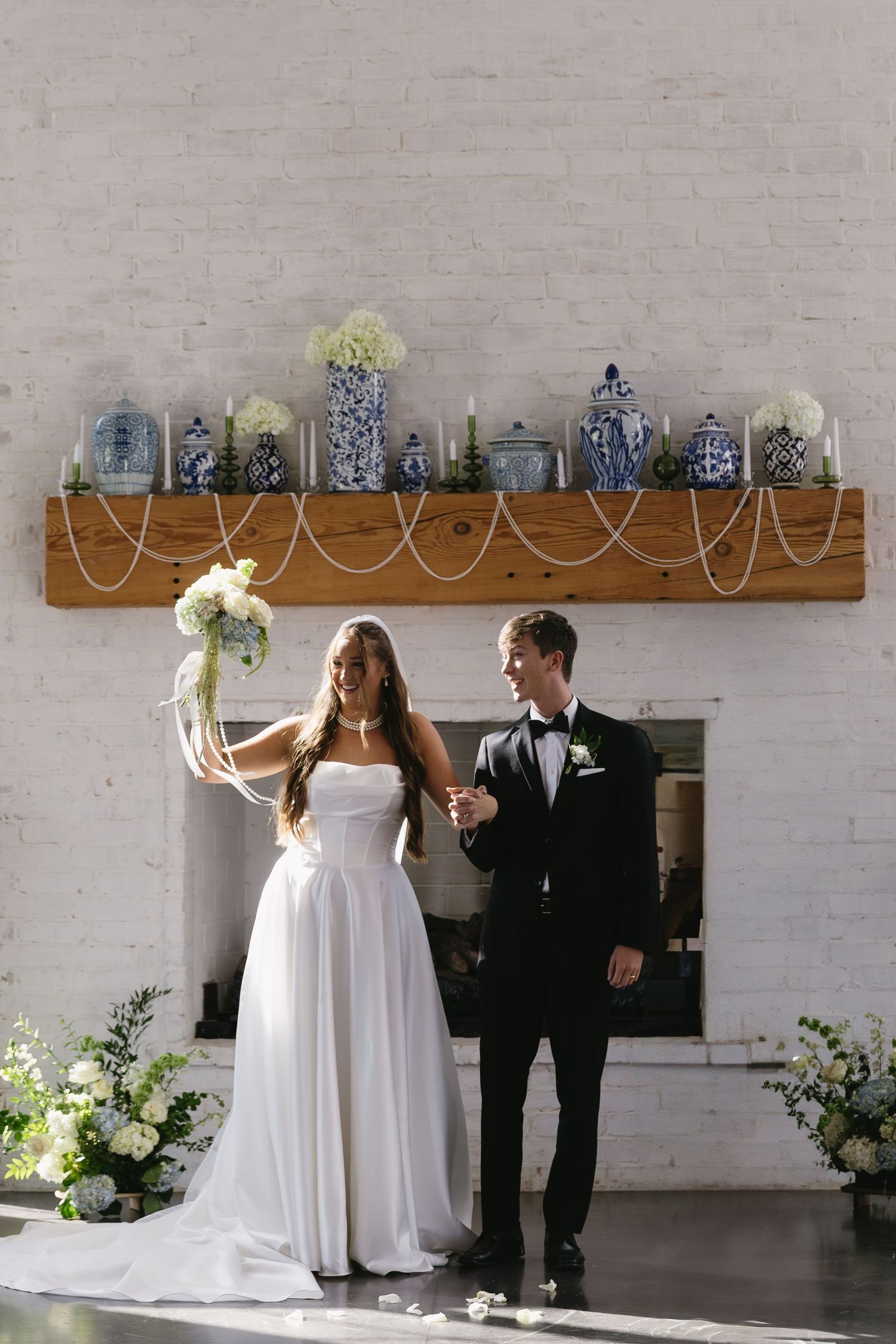 A wedding couple dances in a bright minimalist room with exposed brick walls and decorative shelving.