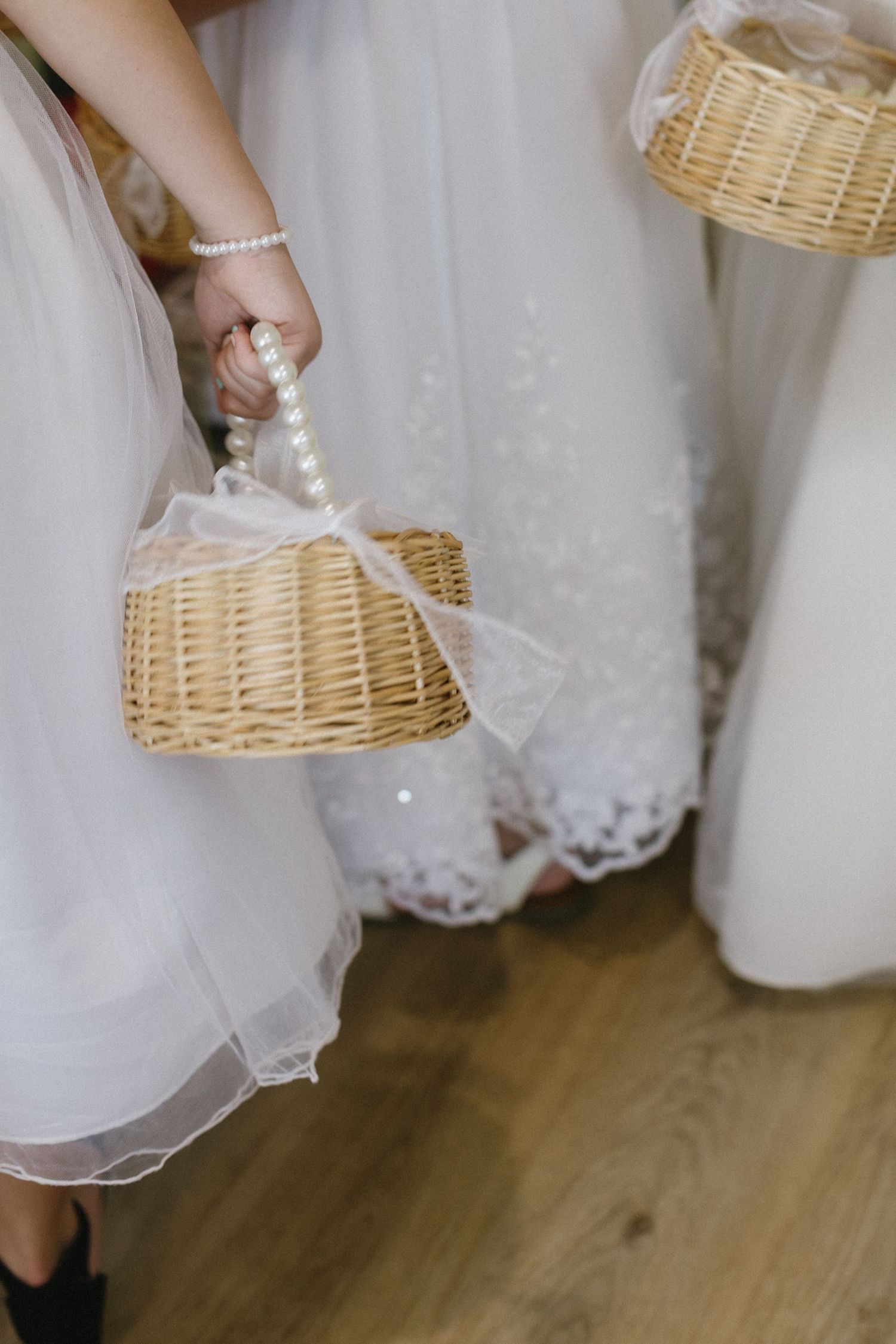 Detail shot of white lace dress hem and wicker basket against wooden floor.