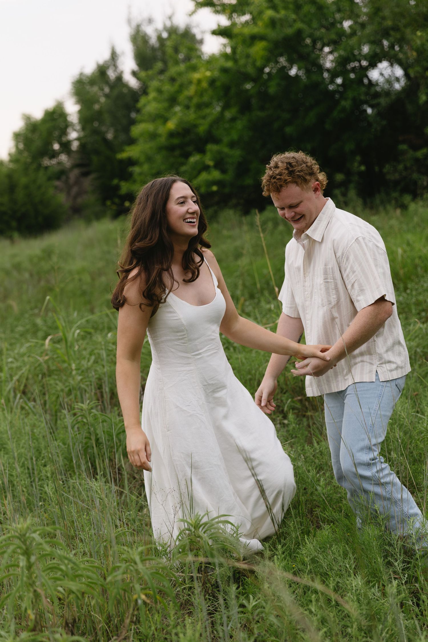 A joyful couple runs playfully through tall grass in a sunny meadow together.