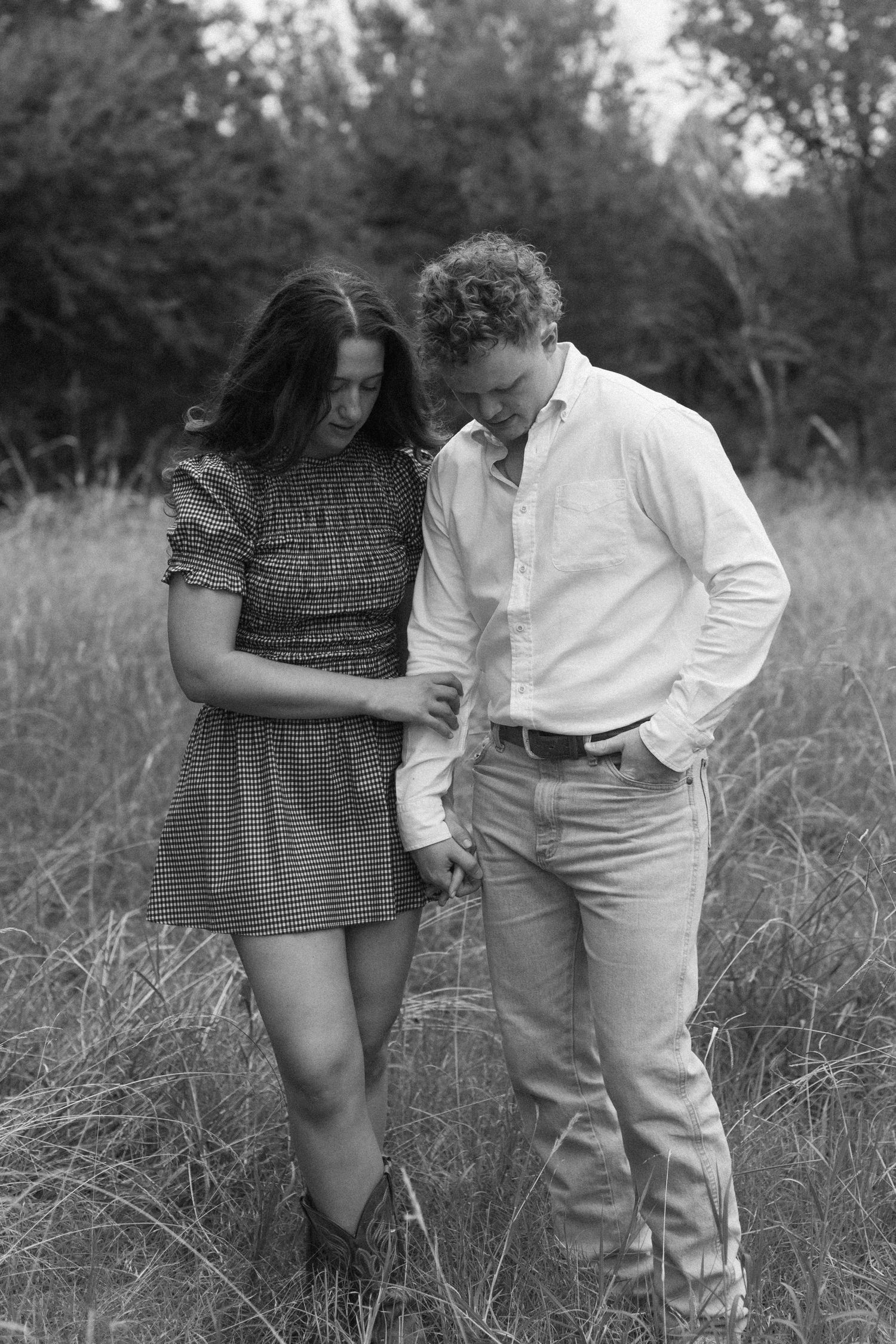 A couple shares a tender moment while walking through tall grass in a natural outdoor setting.