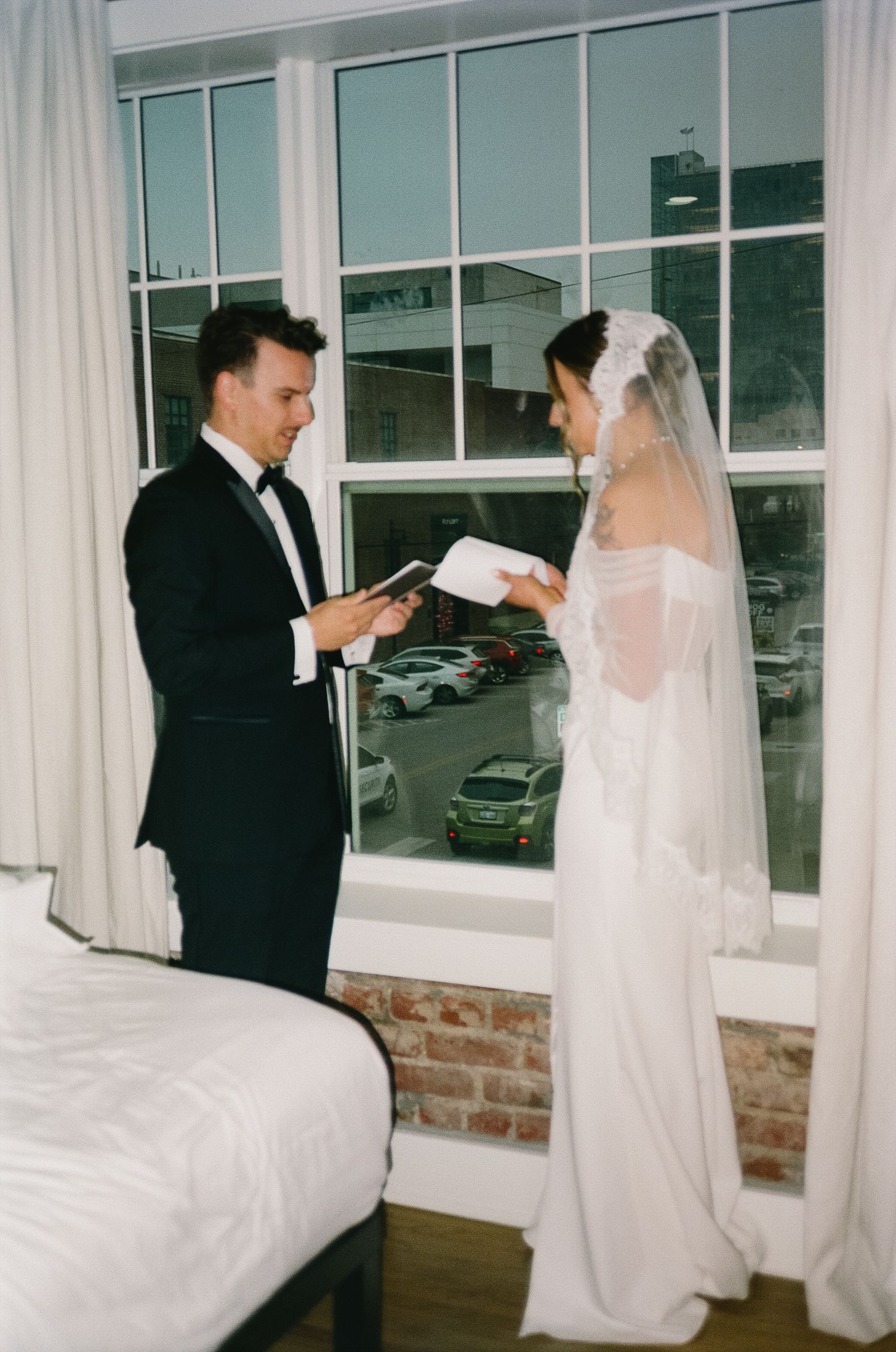 Wedding couple in formal attire sharing a private moment by large windows.