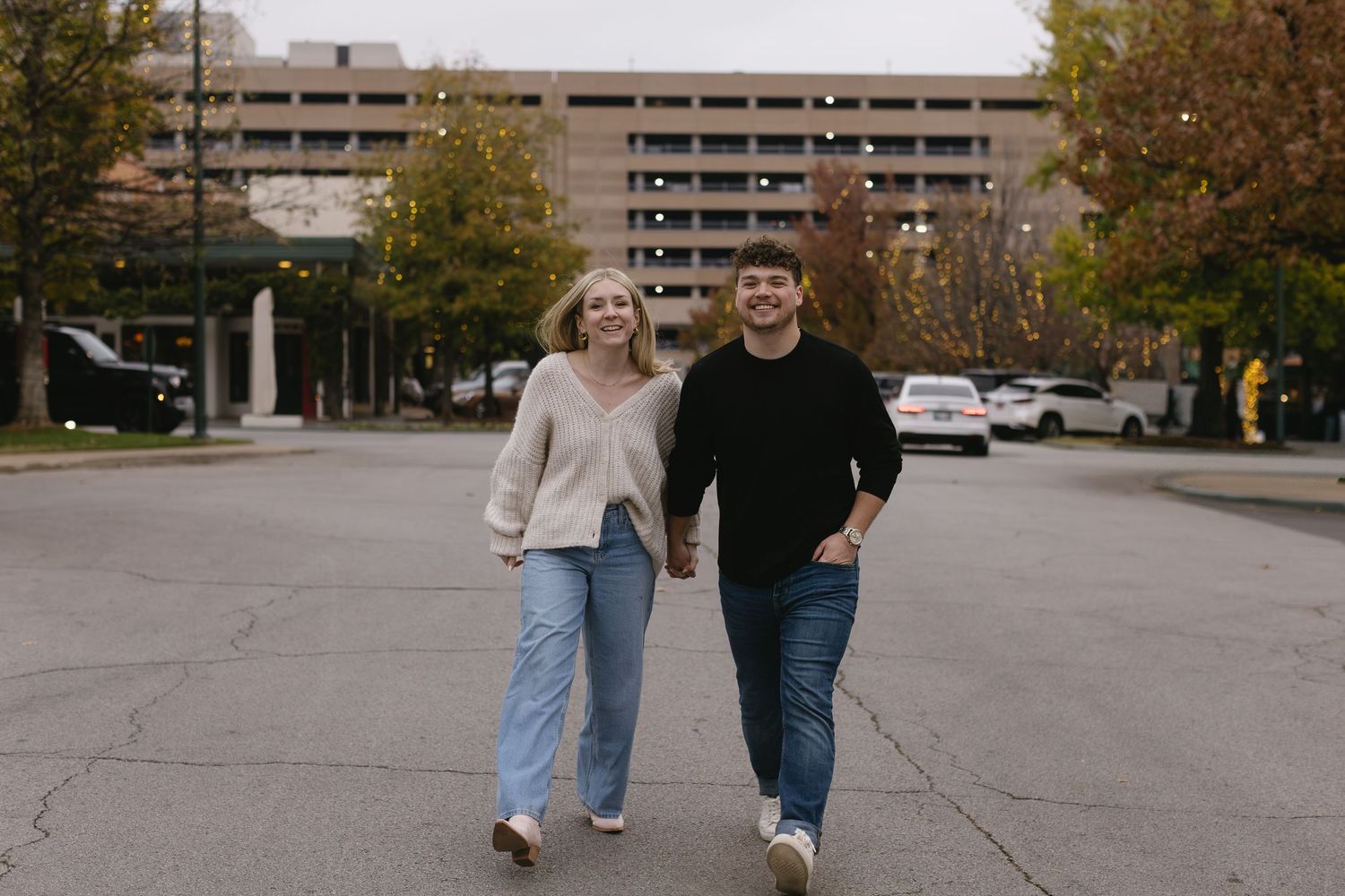 Wide shot of a couple walking together in an urban setting with parking structures.