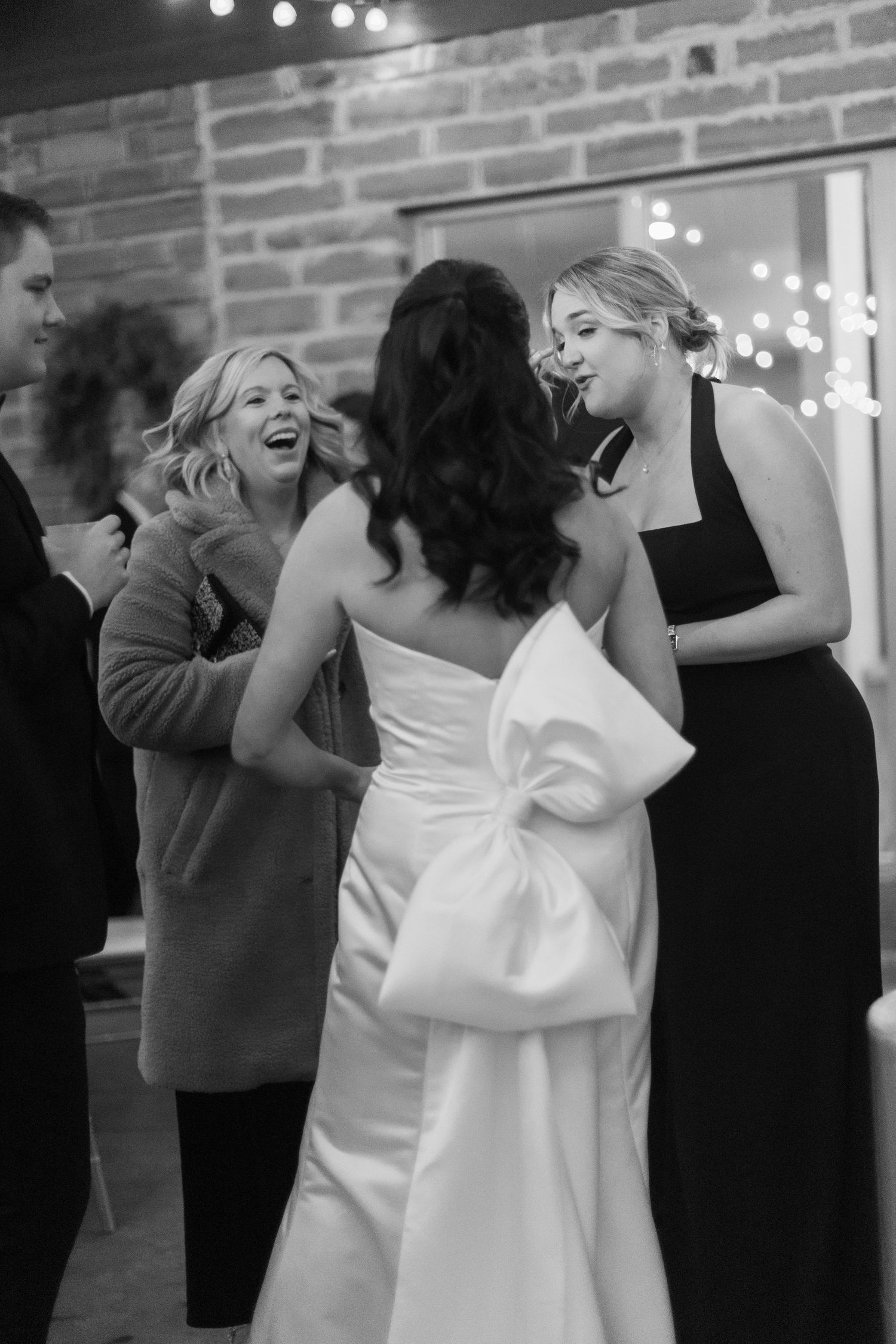 Wedding guests dancing and celebrating at indoor reception with brick wall backdrop.
