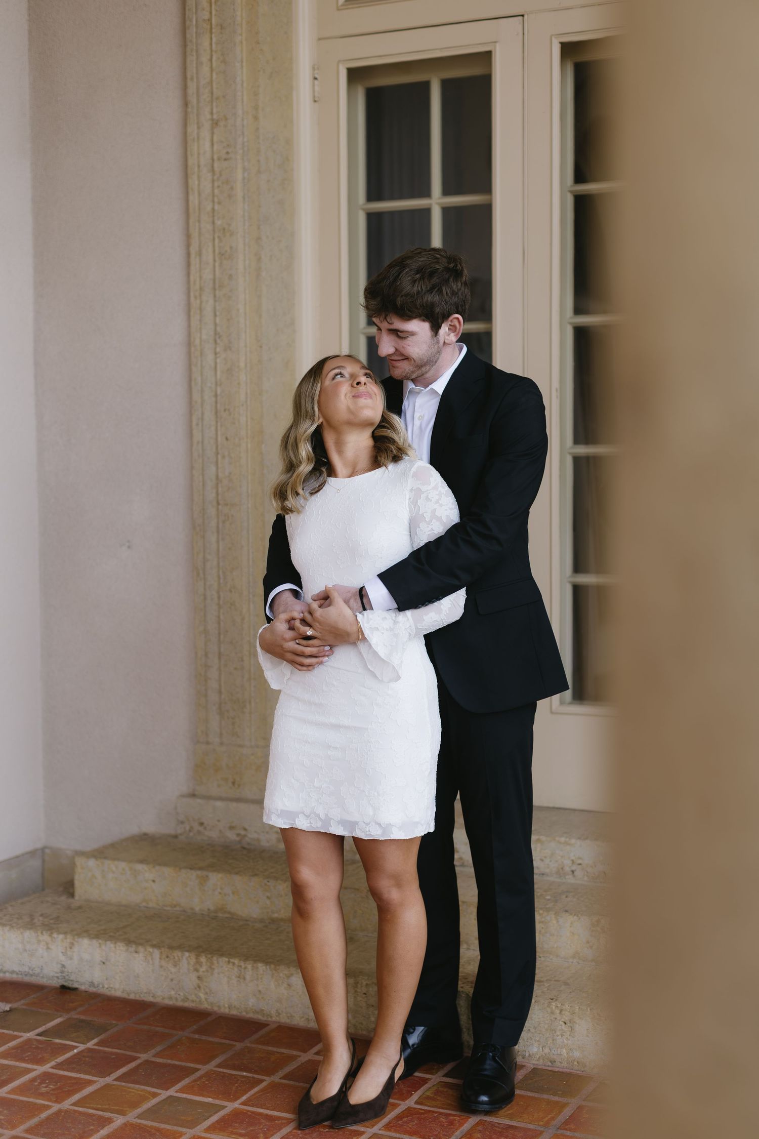 A tender moment between a couple in formal wear standing on stone steps.