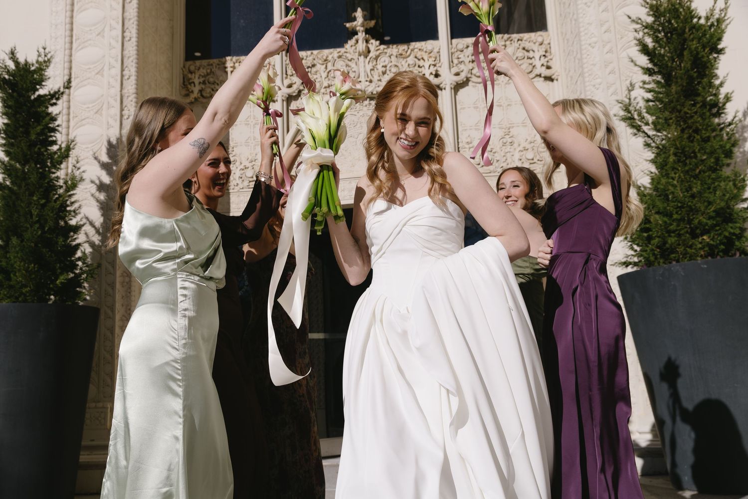 Wedding party in white and purple dresses pose together outside an elegant venue.
