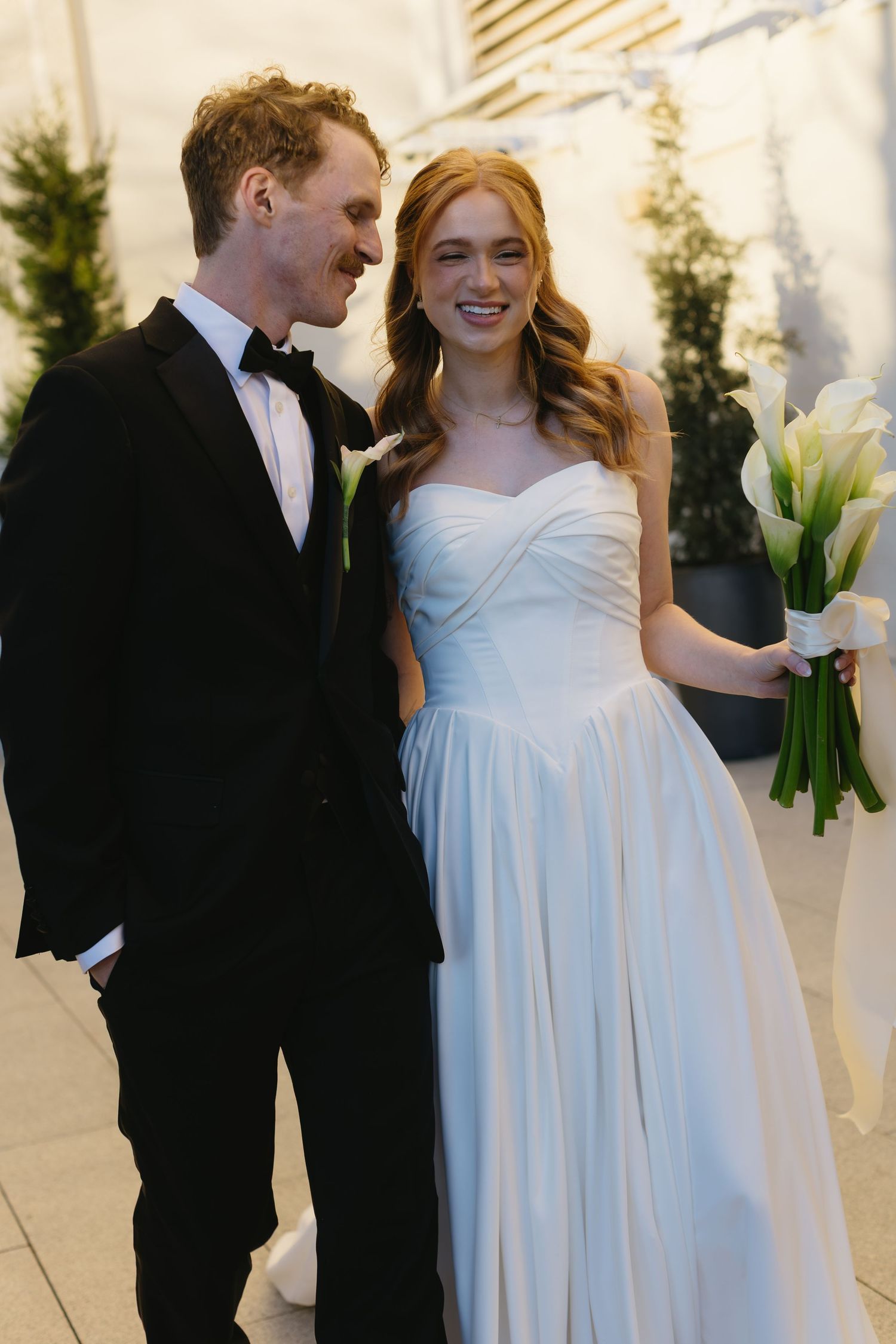 Elegant wedding couple in white dress and black tuxedo with calla lily bouquet.