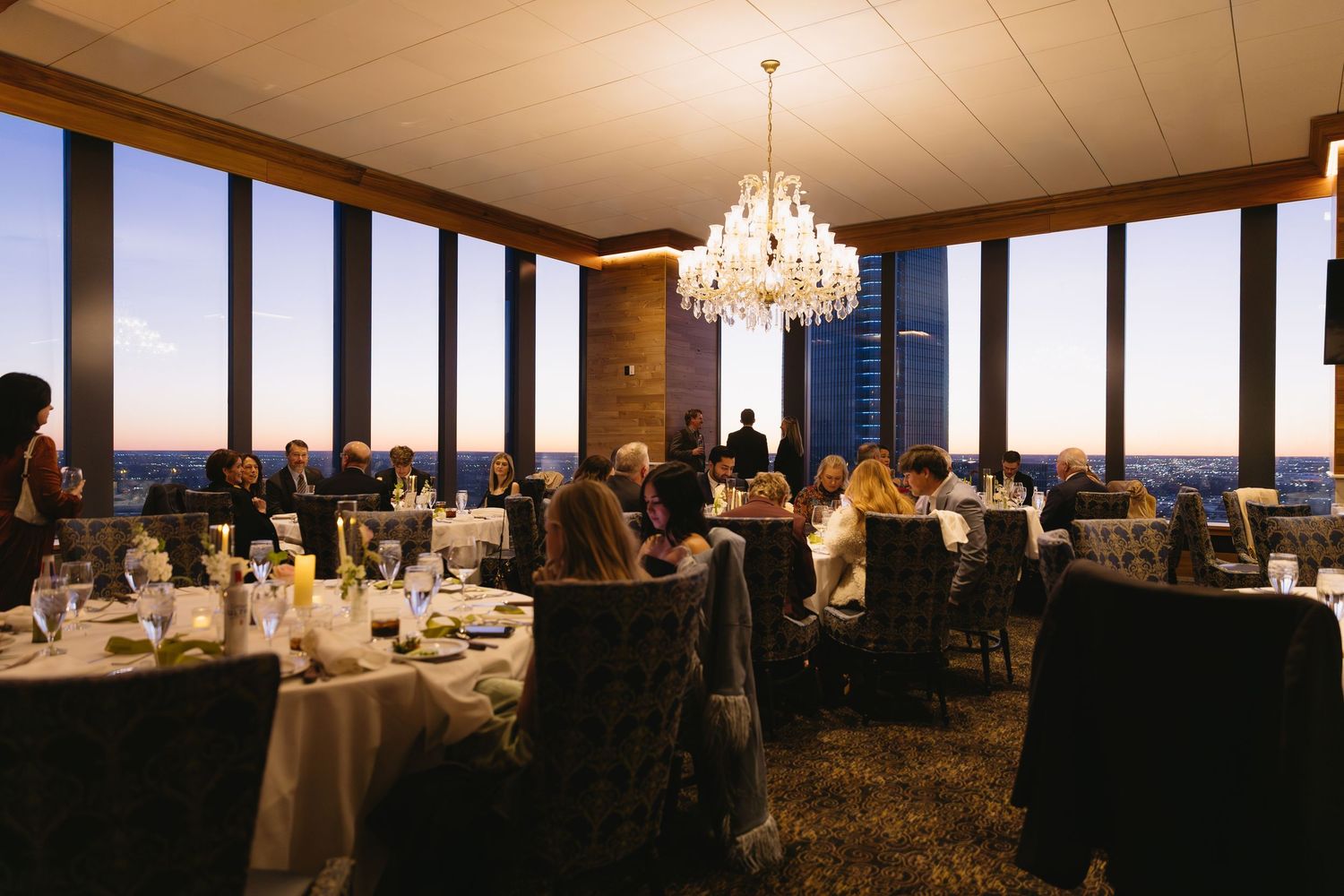 Elegant wedding reception venue with chandeliers and panoramic windows at sunset.