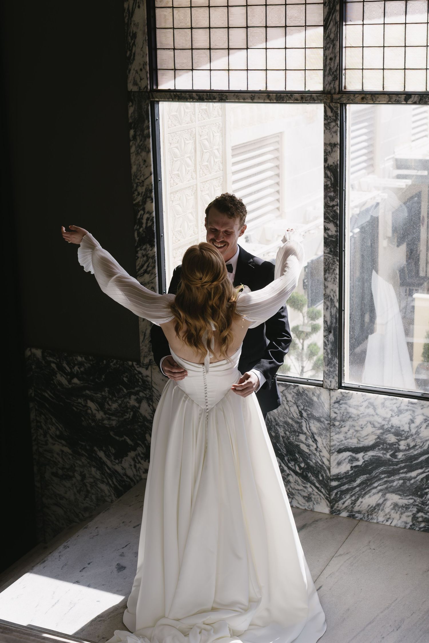 Romantic wedding moment captured near large industrial windows with natural light streaming in.