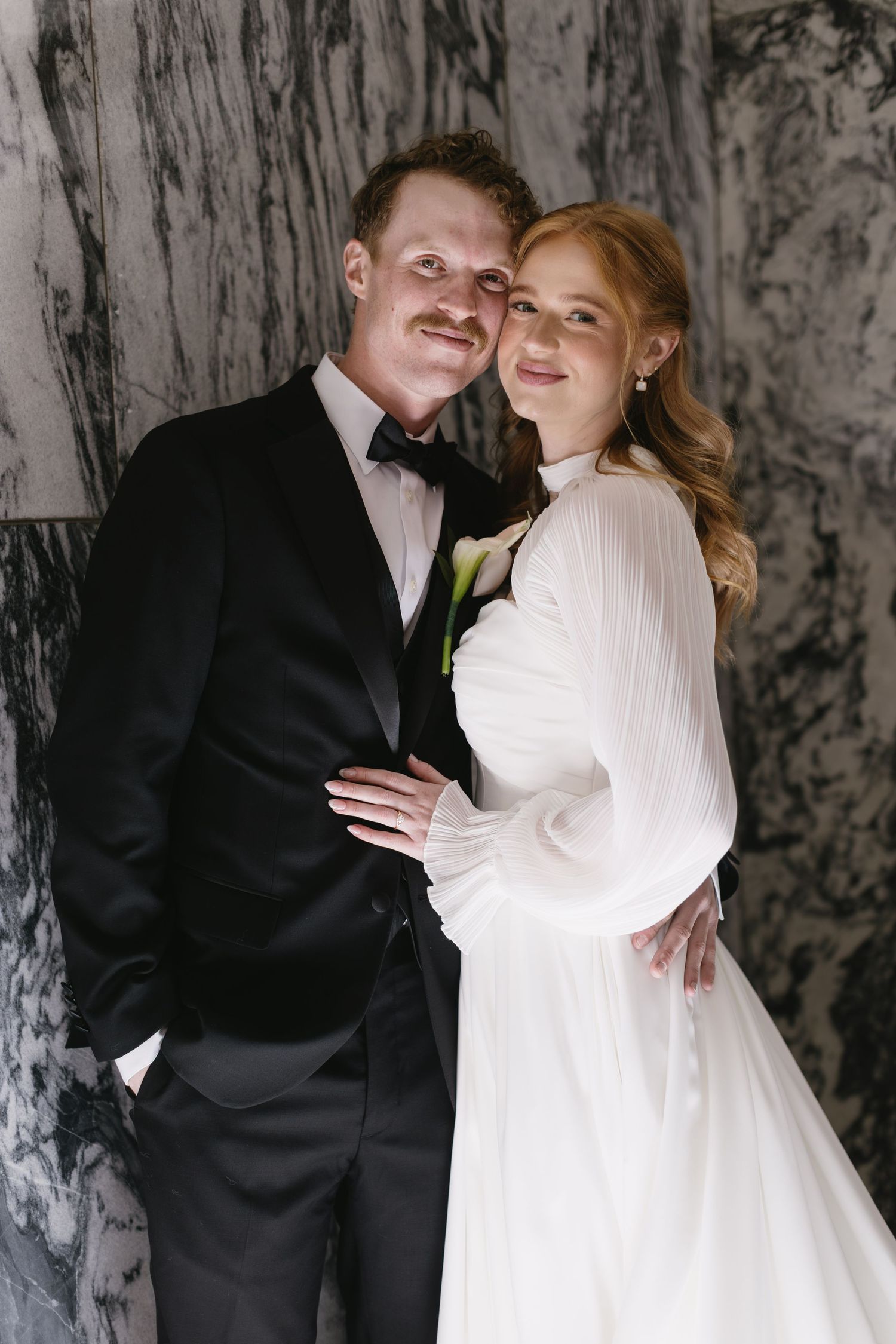 Romantic wedding portraits against textured marble wall with natural lighting.