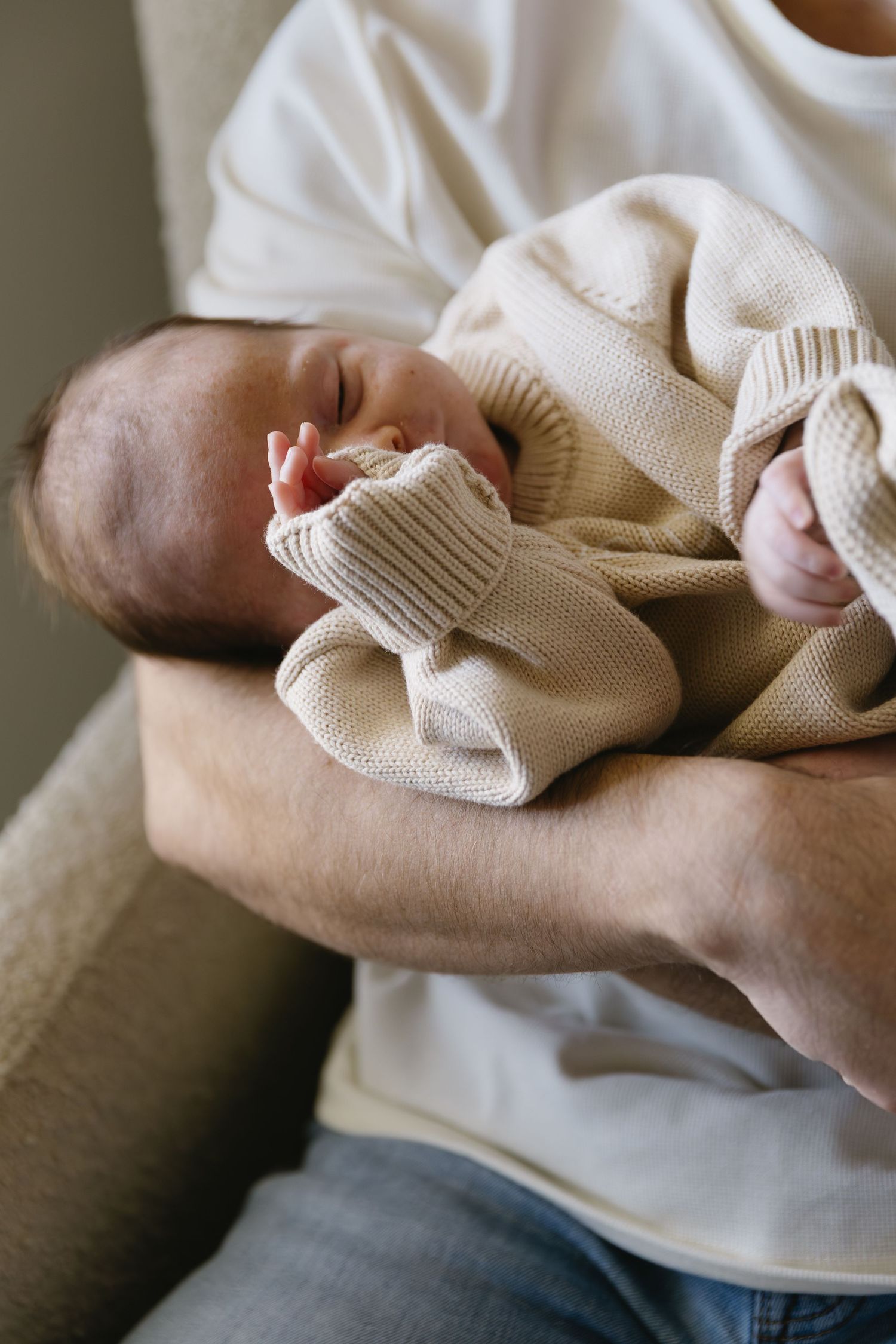 Close-up of hands holding tiny knitted baby socks in beige color.