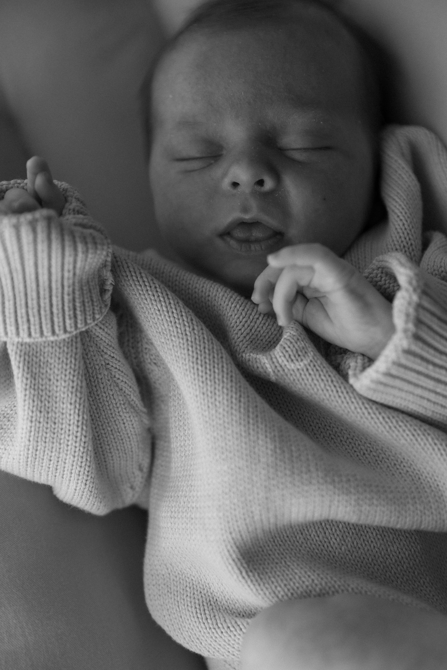 Close-up black and white portrait of a sleeping newborn baby wearing a white knit sweater.