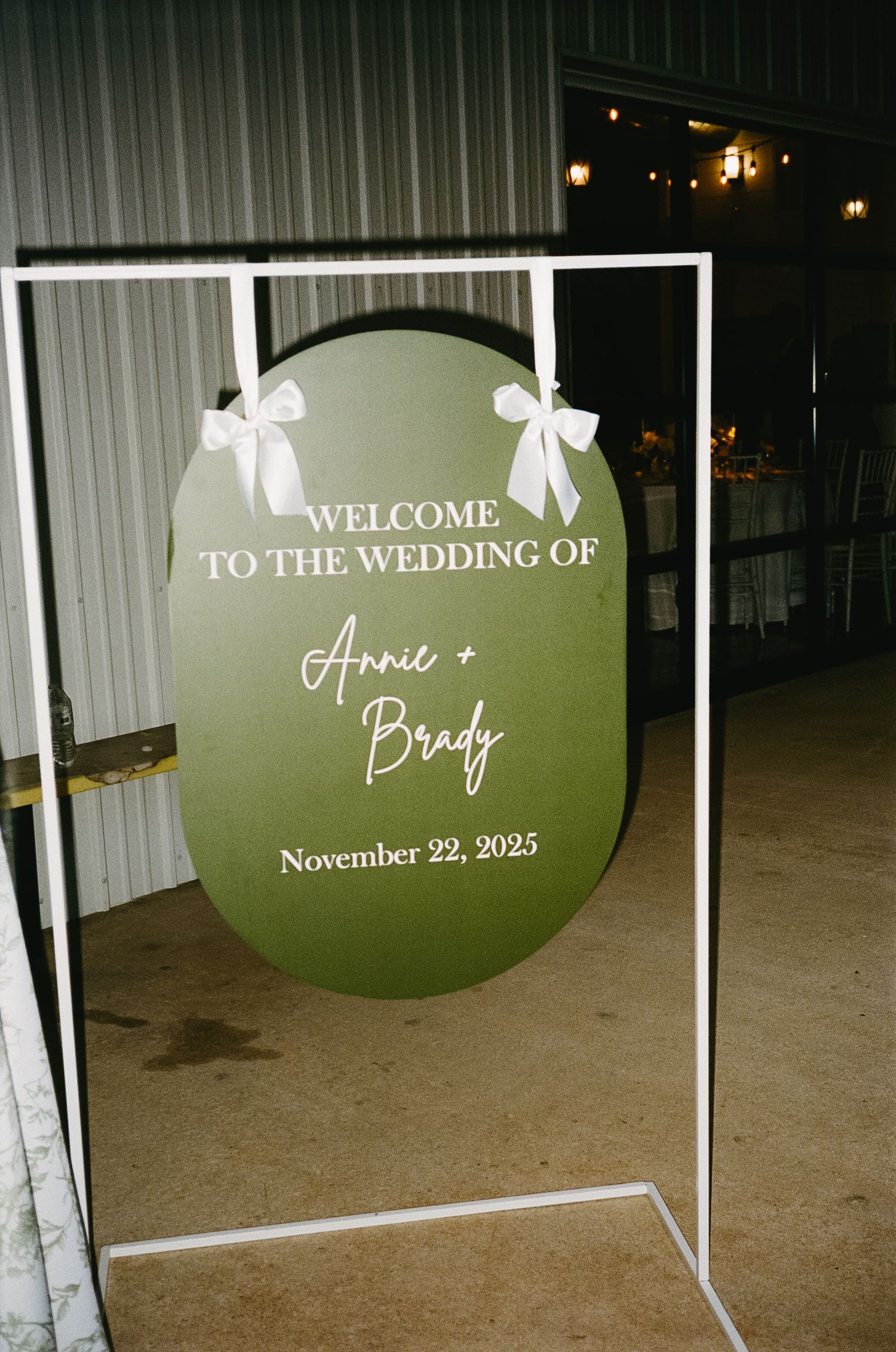 Green and white wedding welcome sign with bows displaying the couple's names and wedding date.