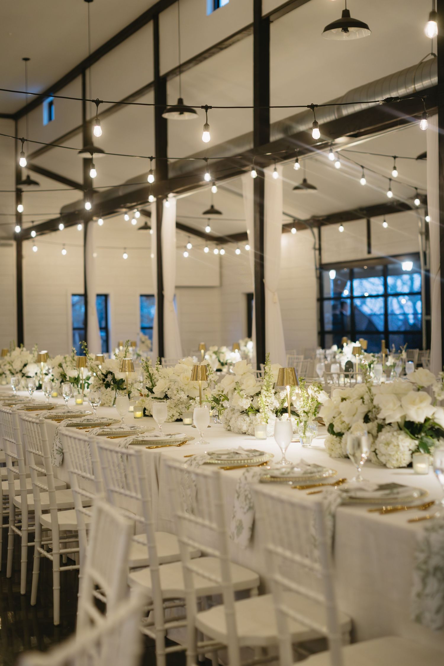 Modern wedding reception venue with white tables and string lights creating an elegant atmosphere.