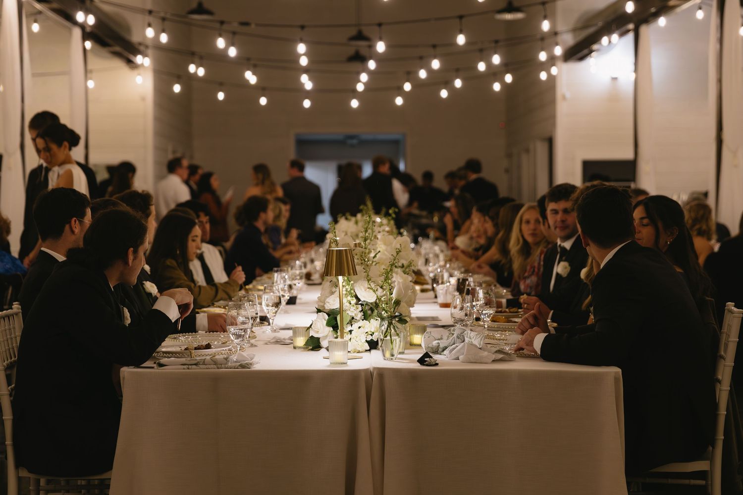 Large wedding reception venue with string lights and white-clothed tables set for dining.