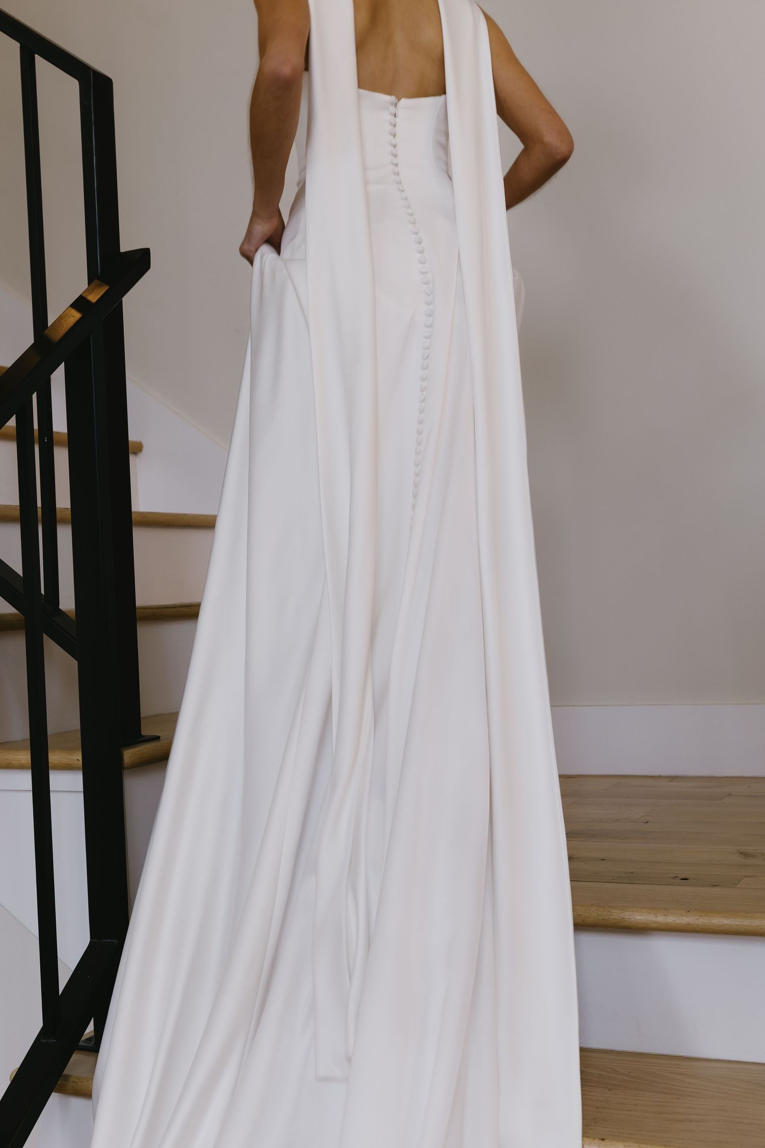 Flowing white wedding dress details showing the skirt and train against light wooden floors.