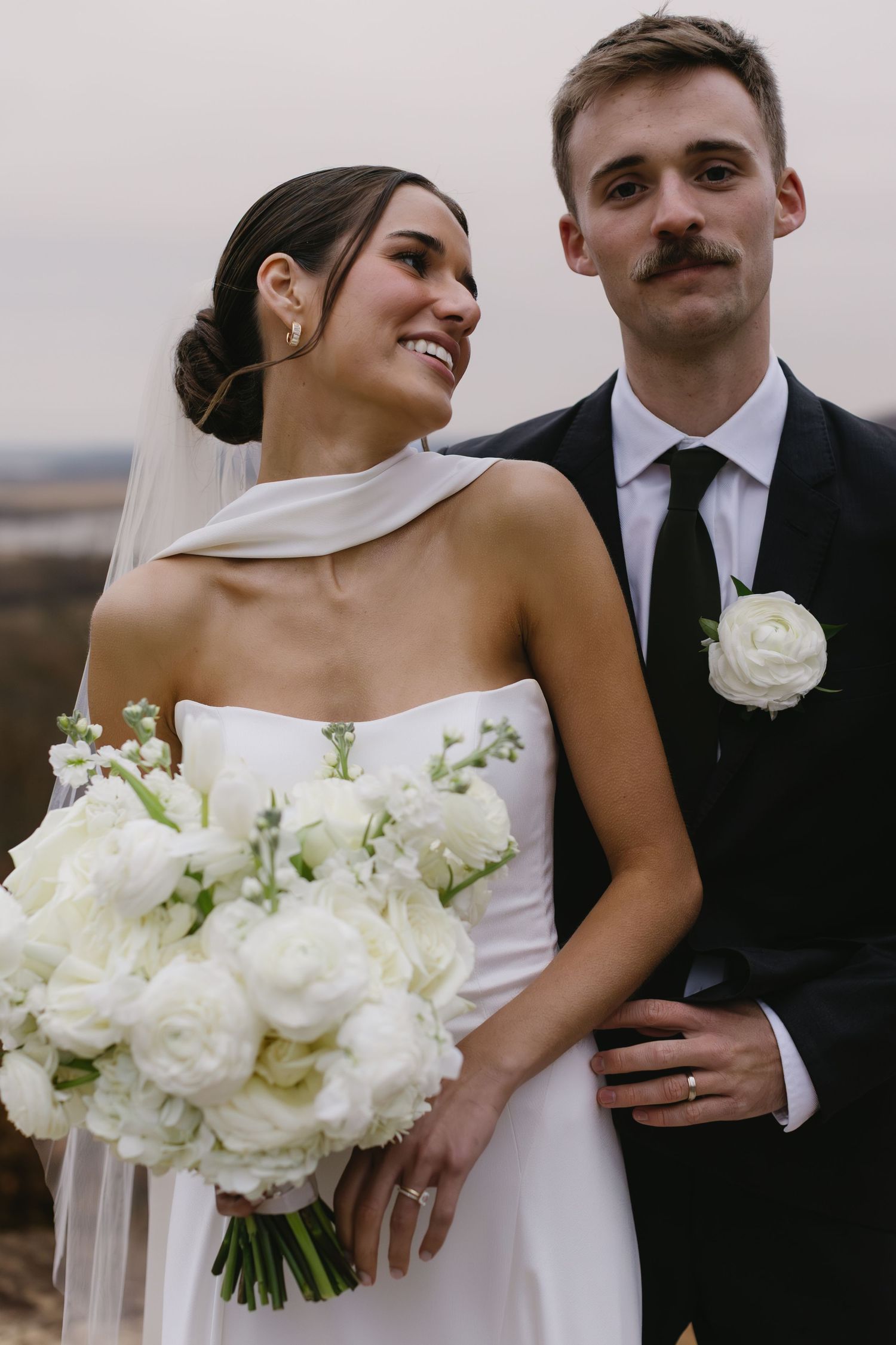 Elegant wedding portraits featuring white bouquet and classic black tuxedo against neutral background.