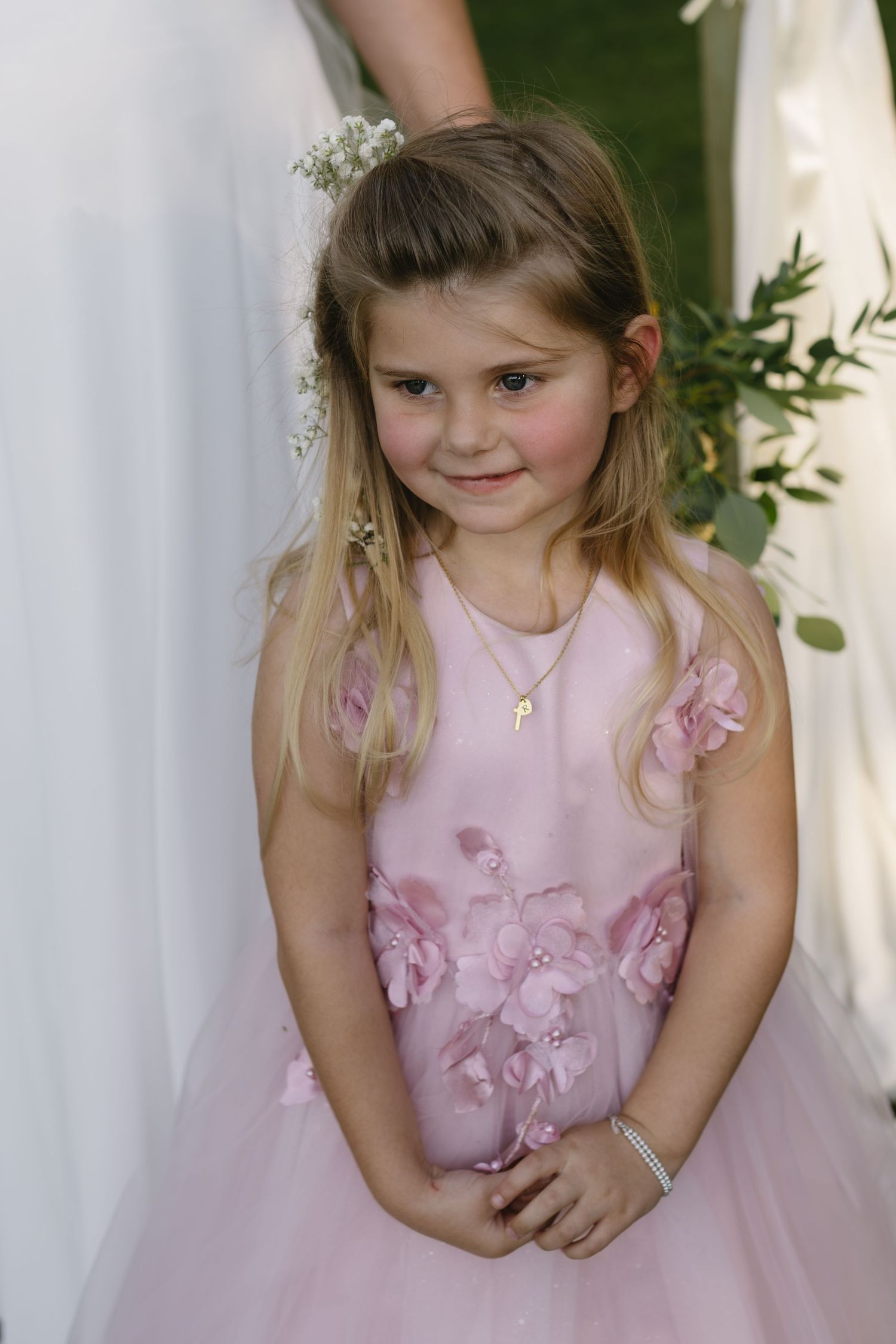 A young attendant in a pink dress poses during a wedding celebration outdoors.