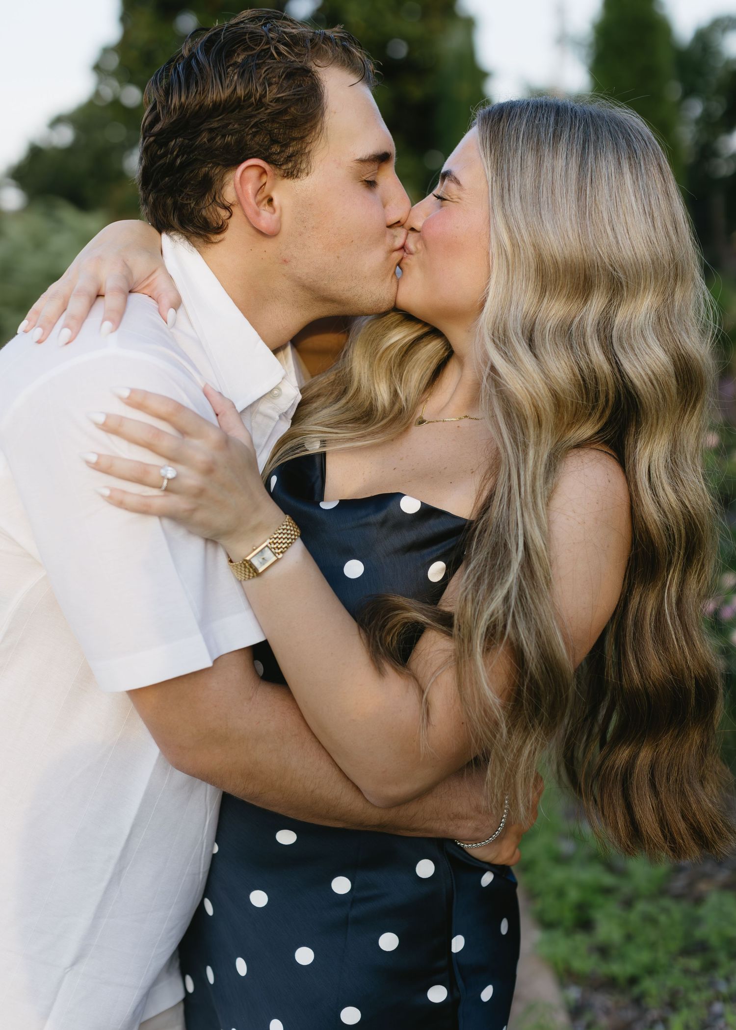 Romantic couple embraces in a passionate kiss outdoors, the woman wearing a polka dot dress and the man in white.