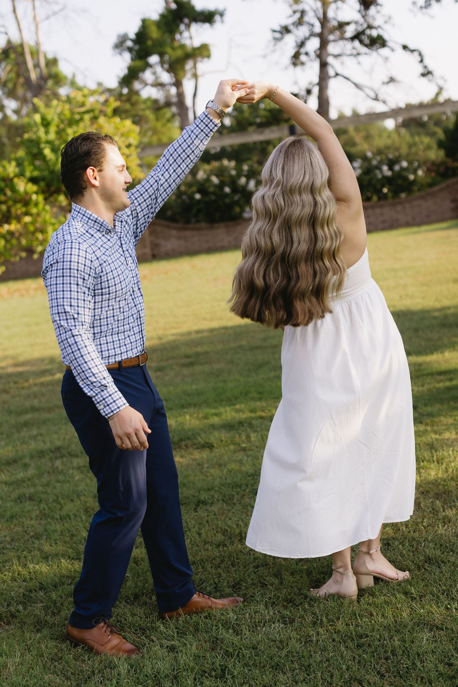 Playful dance moves on a grassy lawn with flowing white dress and checkered shirt creating a joyful scene.