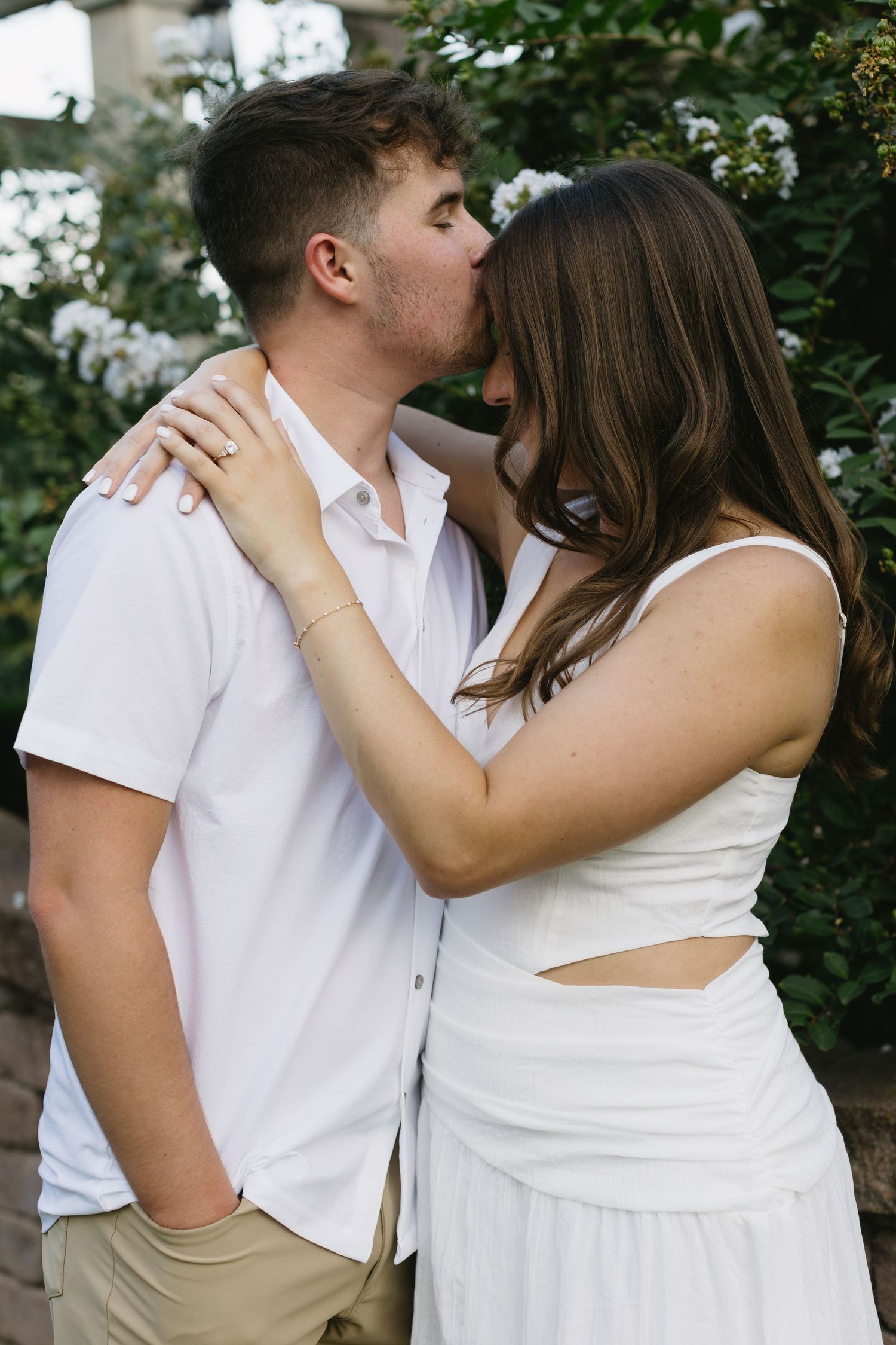 A romantic couple sharing a tender kiss in a garden setting with white flowers in the background.