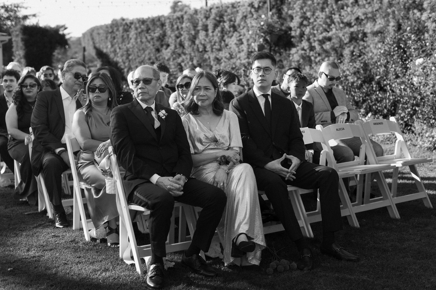 Wedding guests seated outdoors on white chairs during an elegant garden ceremony.