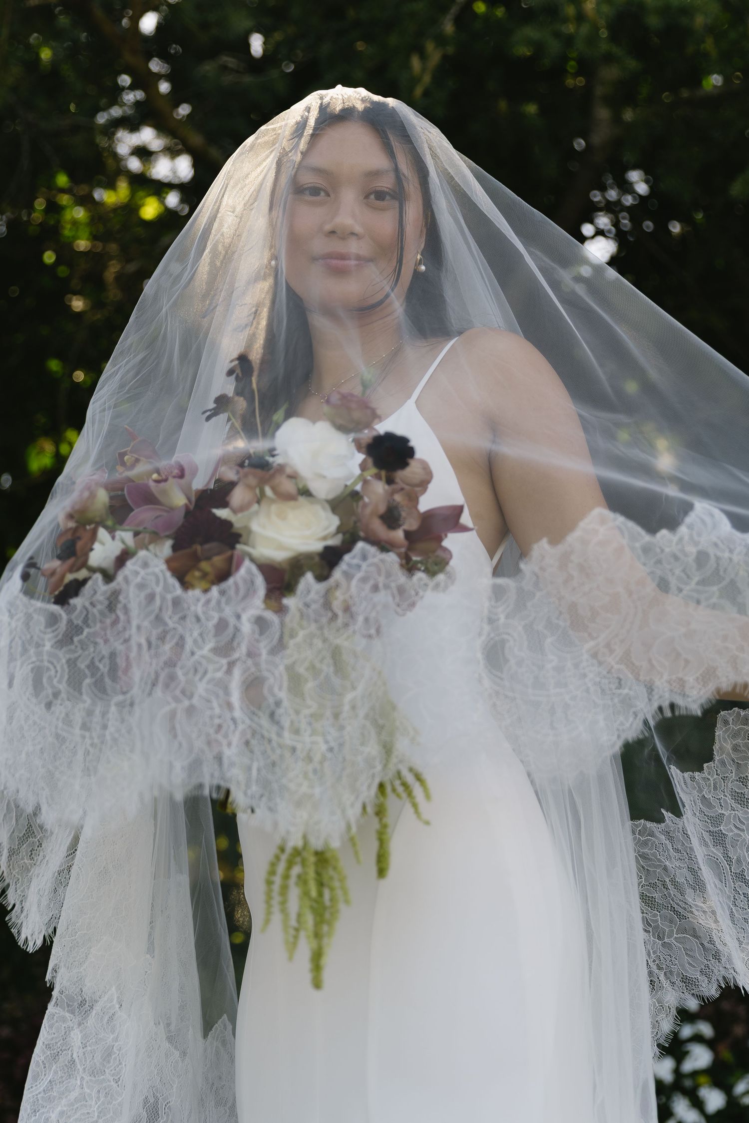 An elegant bridal veil with lace trim frames a beautiful floral bouquet.