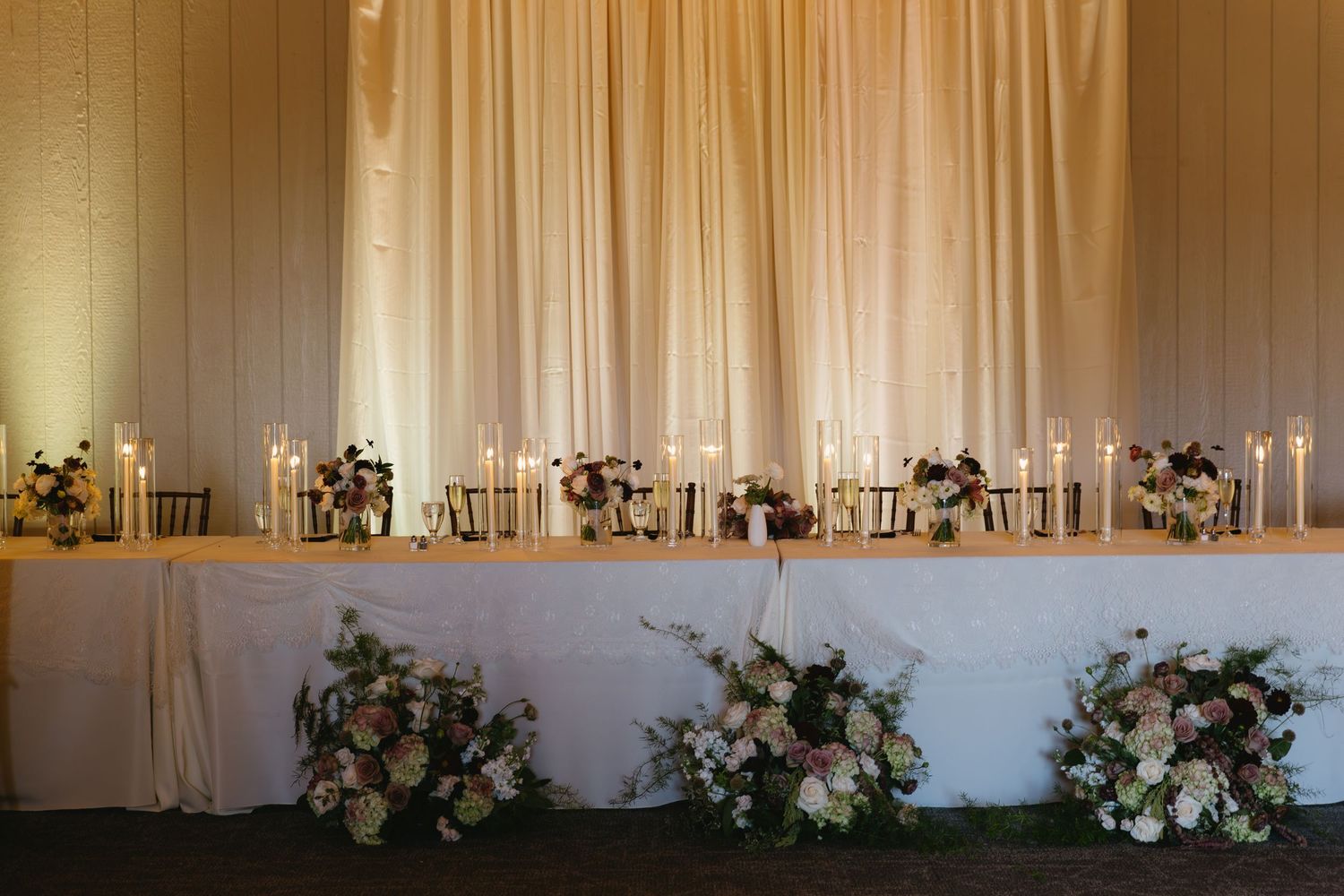 Elegant white draping and floral arrangements decorating wedding reception venue.