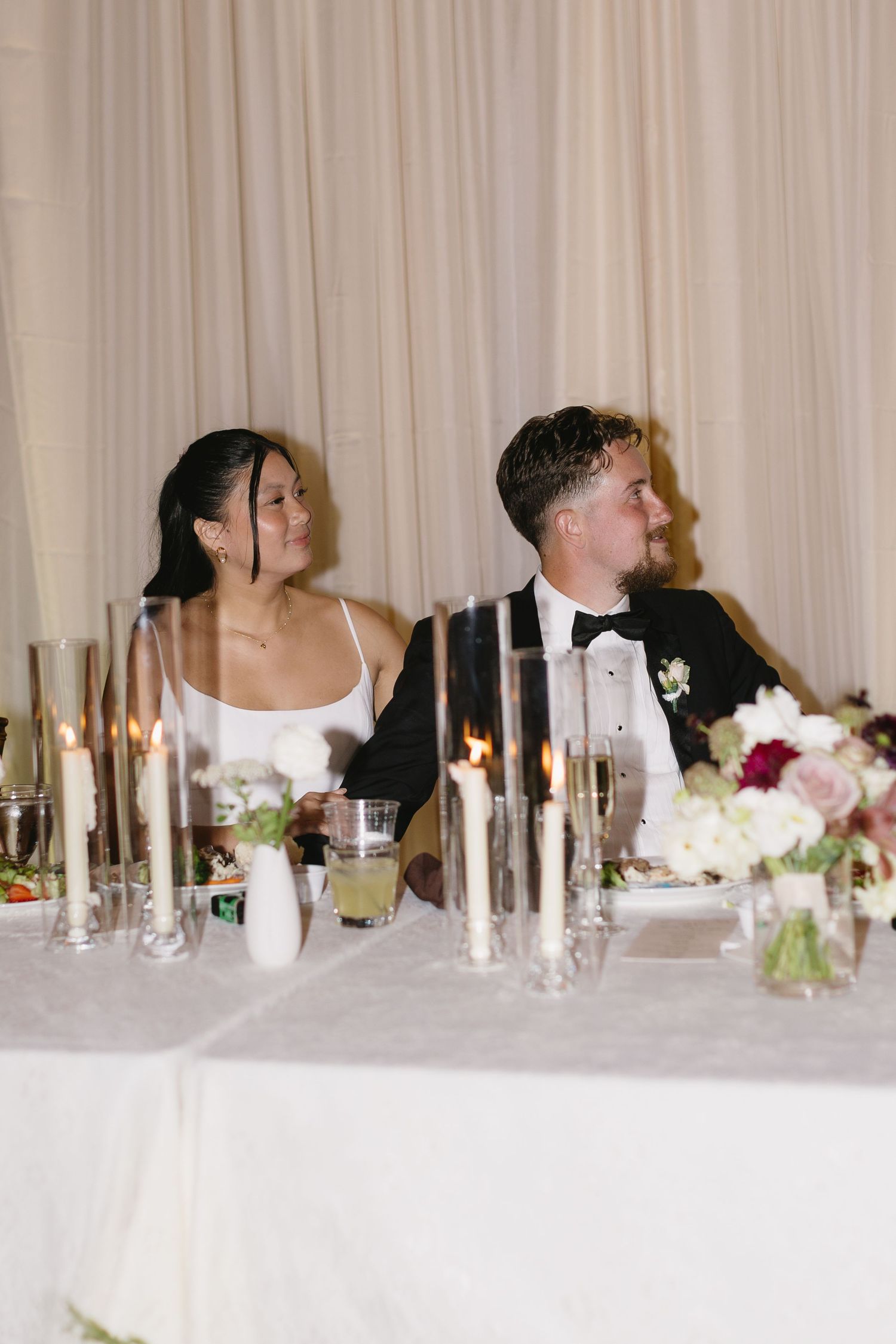 Wedding reception table with white taper candles and floral arrangements against cream backdrop.