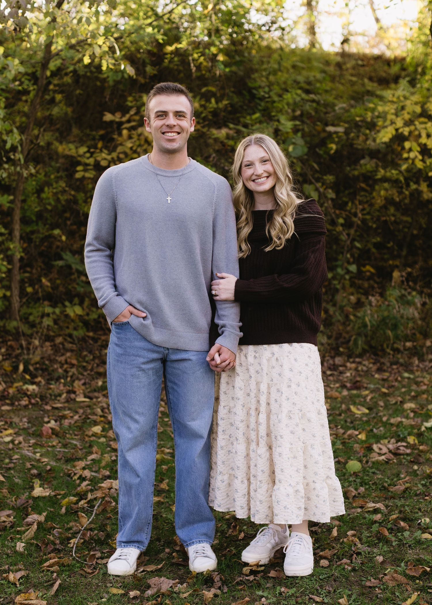 A couple poses playfully in an outdoor setting wearing coordinated outfits of gray and white.