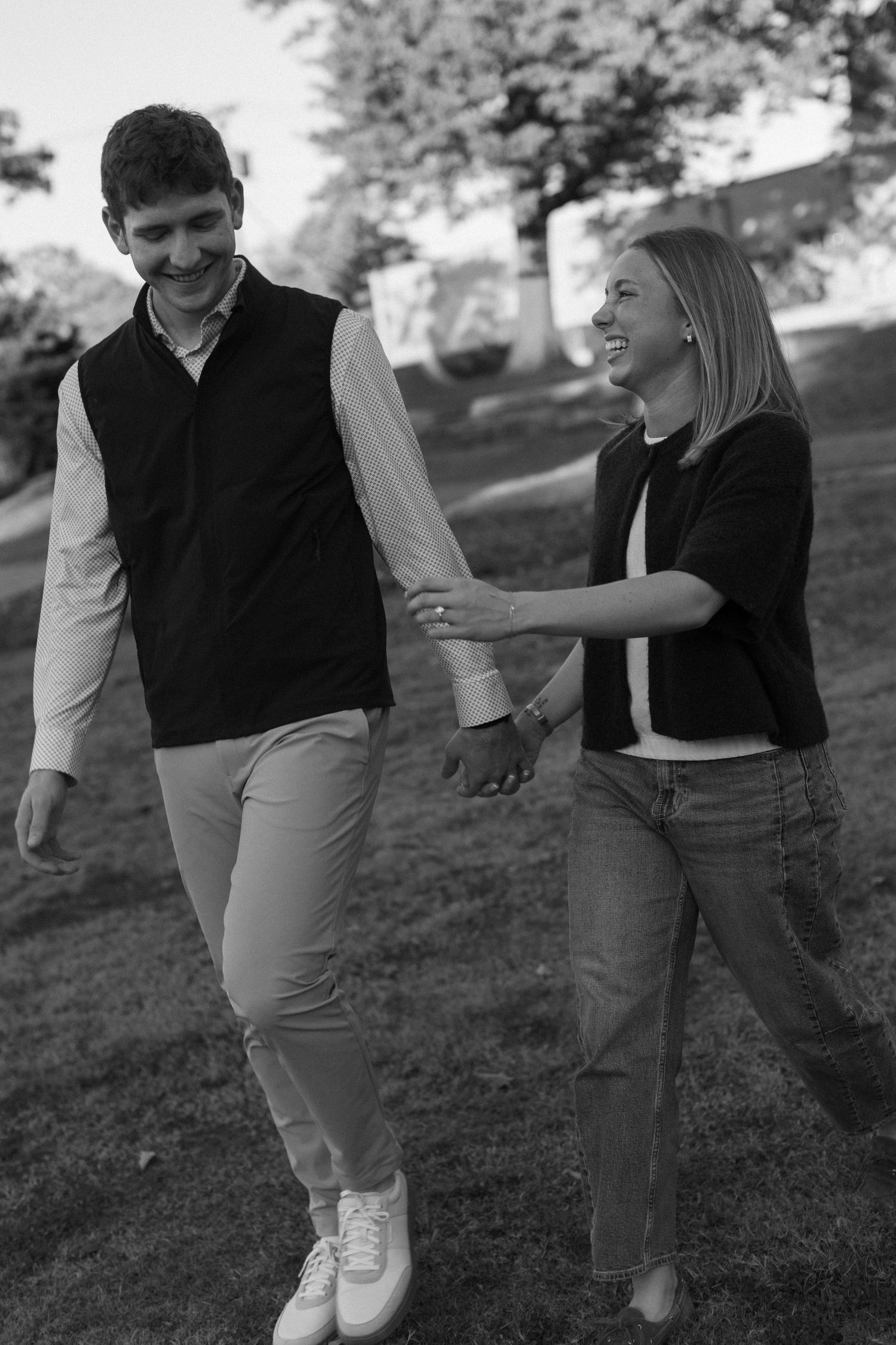 Black and white photo of a playful couple walking and laughing together on a grassy hill.