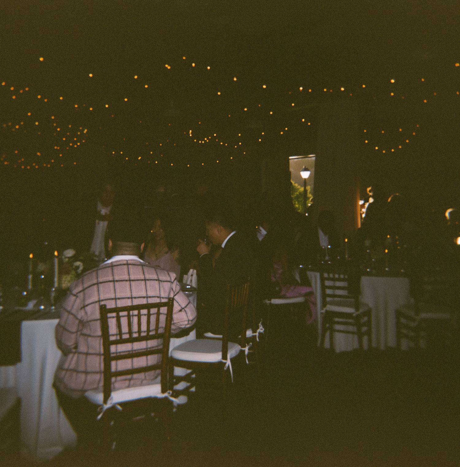 Outdoor wedding reception at night with twinkling lights and wooden chairs creating a romantic ambiance.
