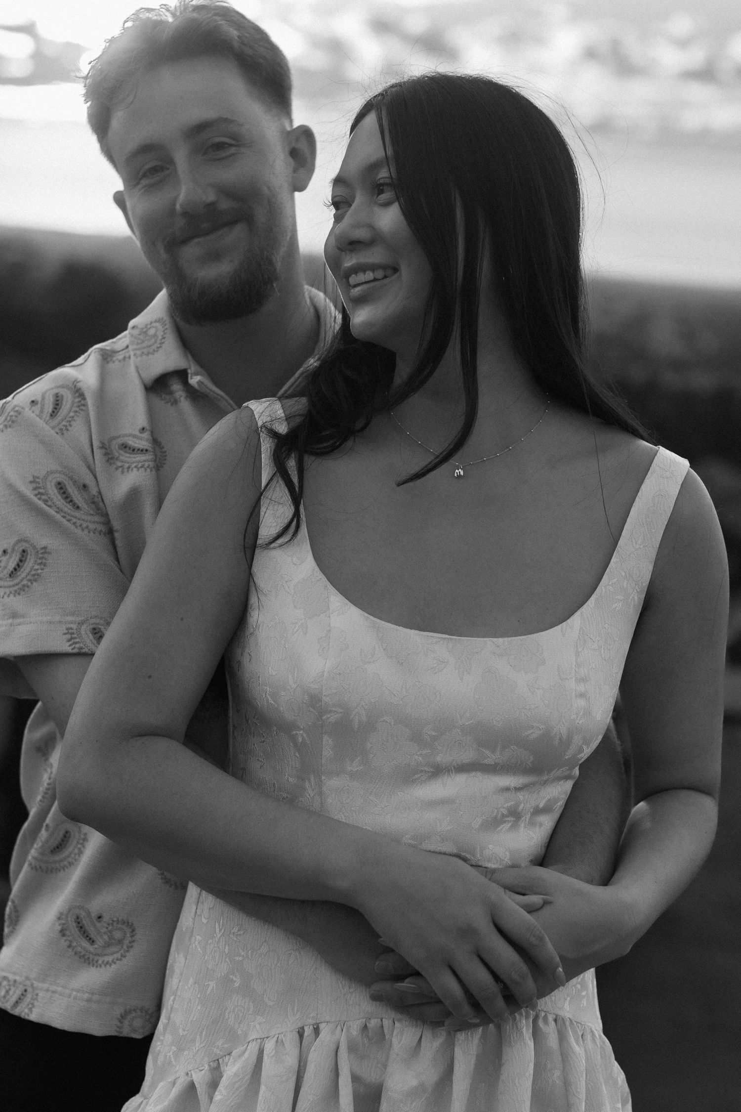 A couple embraces and laughs together during a black and white outdoor photoshoot.