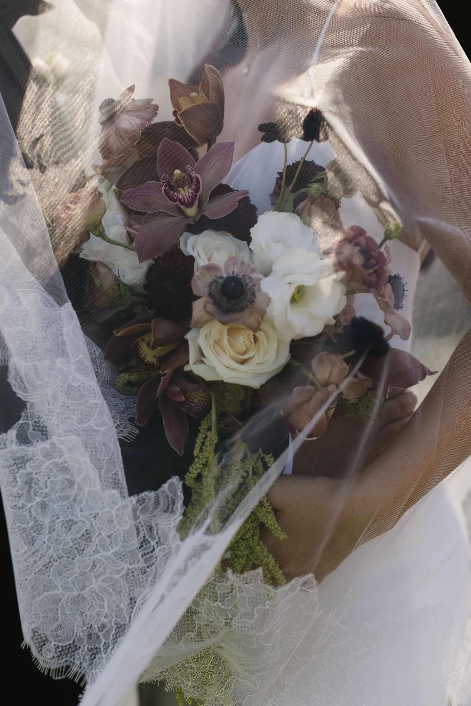 Detailed shot of a bridal bouquet featuring purple orchids, white roses, and delicate lace veil accents.