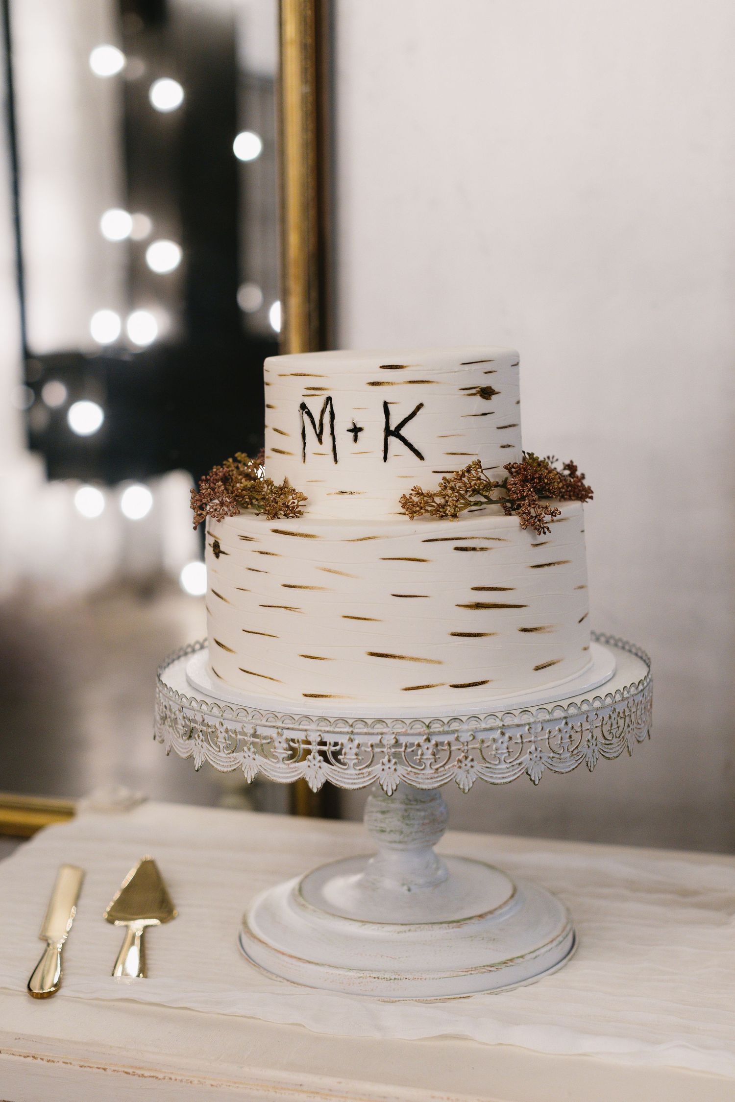 White birch-themed wedding cake with initials M+K displayed on an elegant glass cake stand.