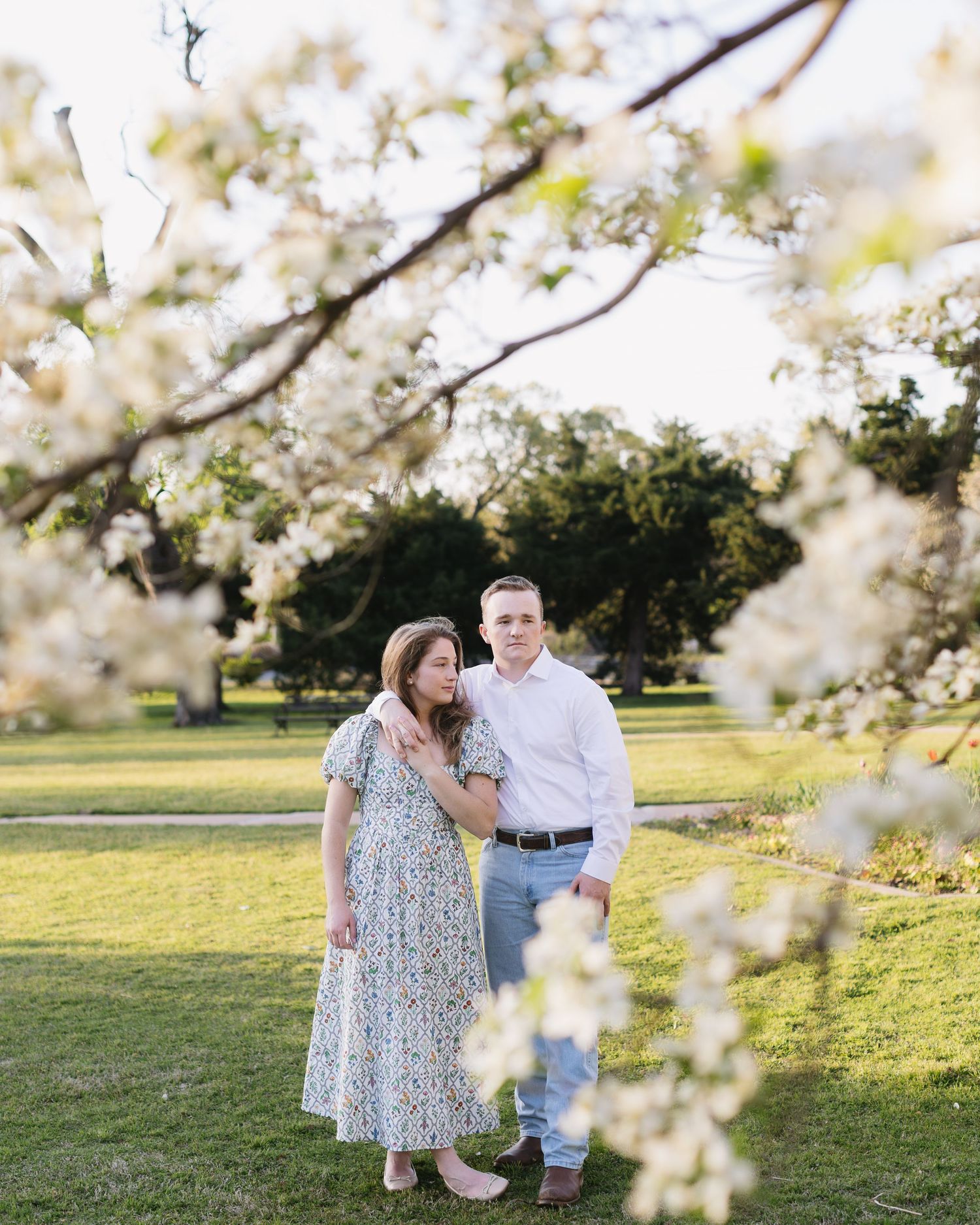A romantic springtime photoshoot under flowering trees with soft sunlight filtering through.