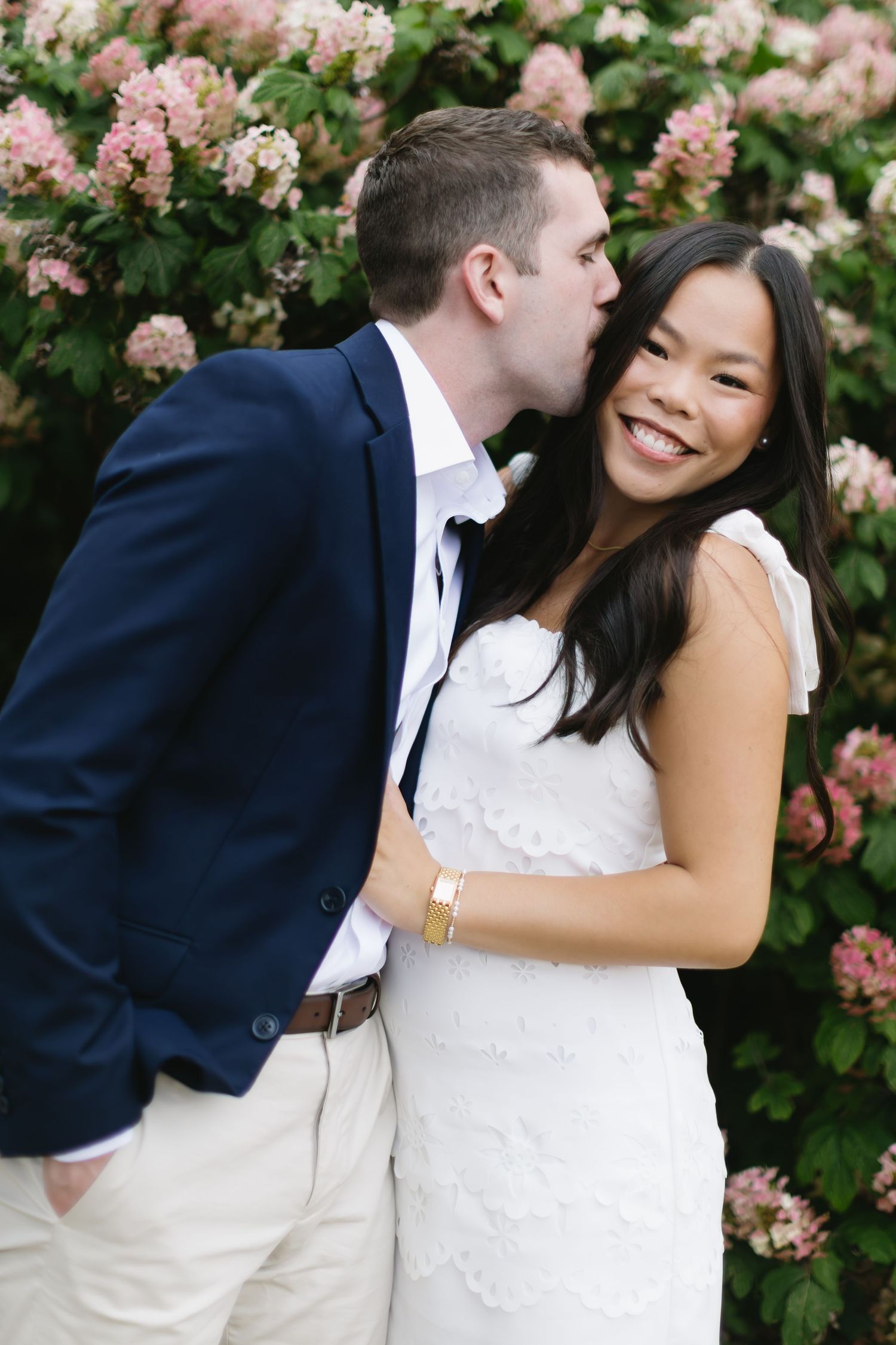 Wedding couple poses playfully in front of blooming pink hydrangea bushes.