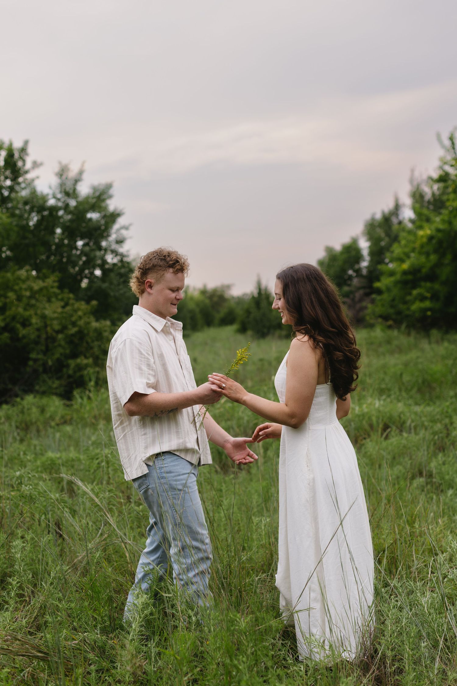 A couple dances and holds hands in a natural meadow setting at sunset.