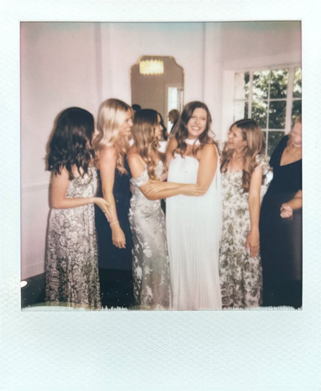 A group of guests dancing and celebrating at a wedding reception wearing floral print and dark dresses.