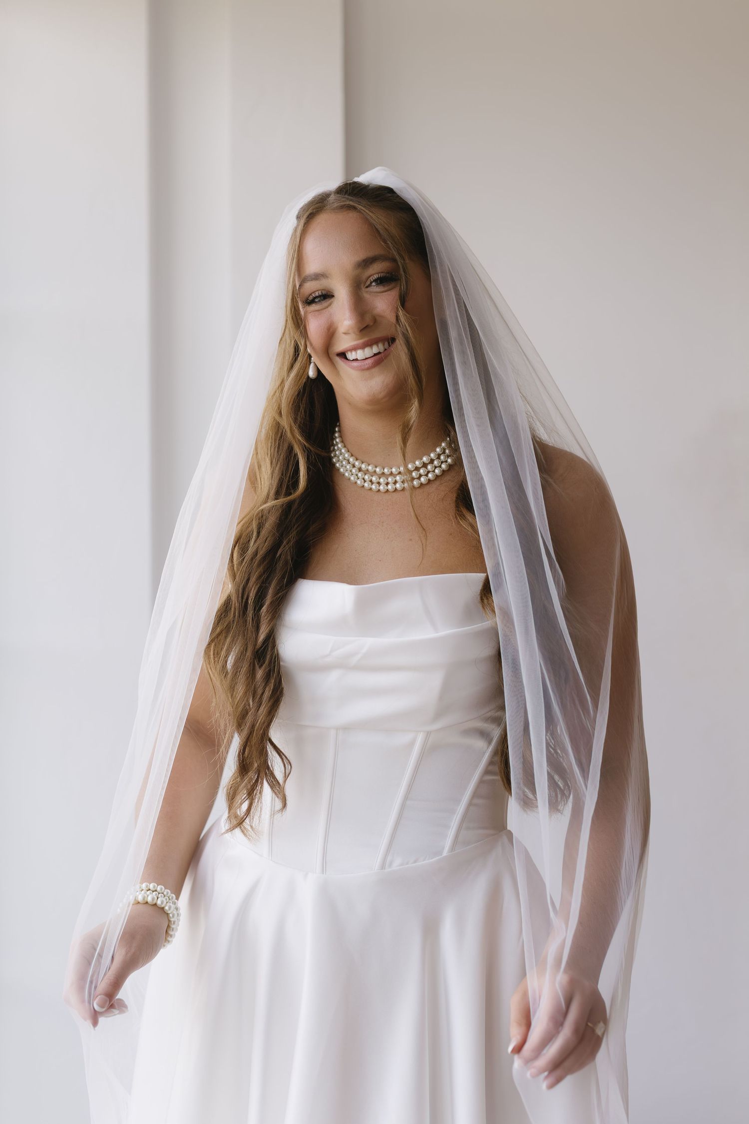 Bridal portraits showing a traditional white wedding dress with strapless neckline and flowing veil against light background.