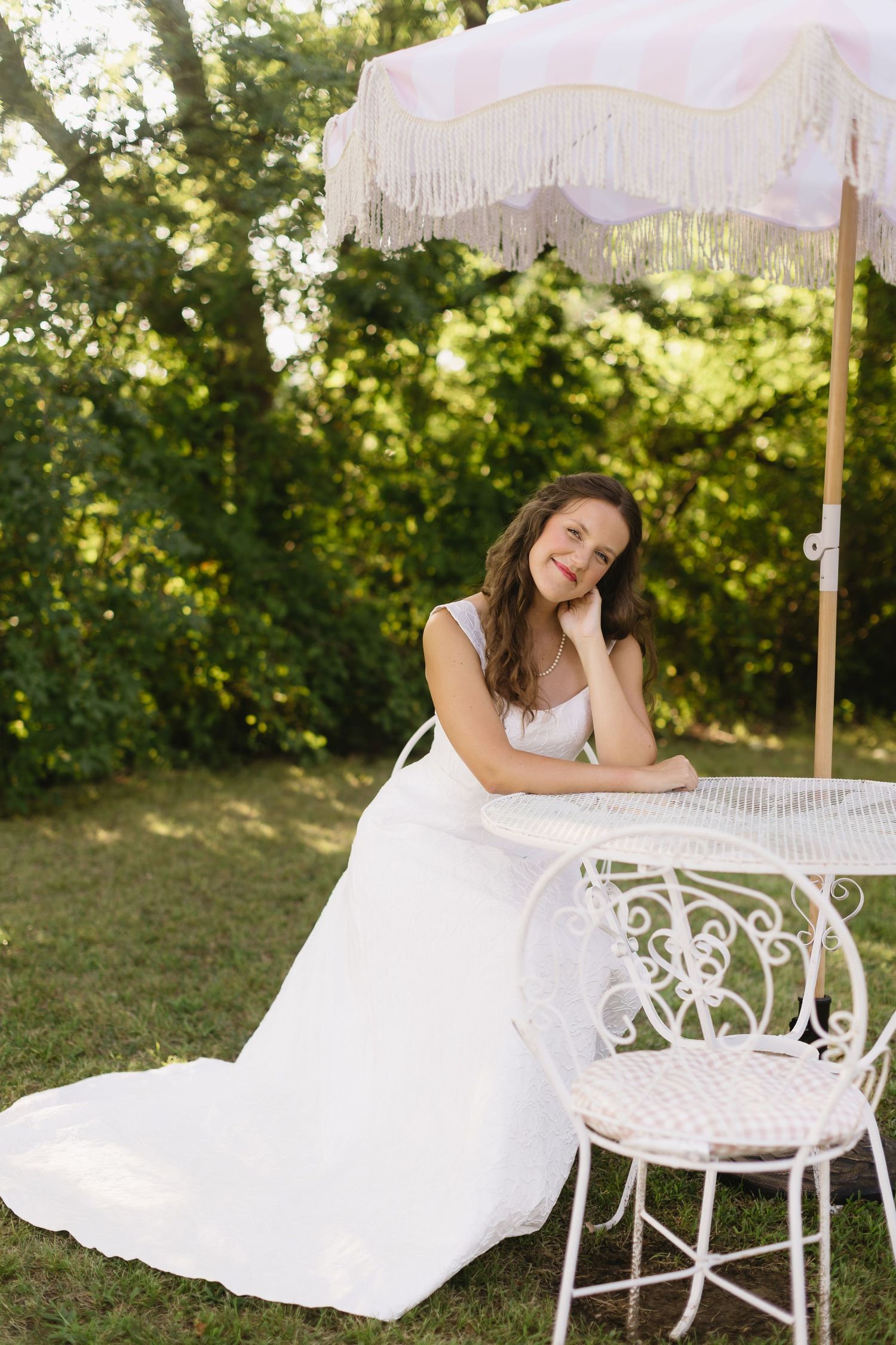 A romantic bridal portrait under a white fringed umbrella in a sunny garden setting.