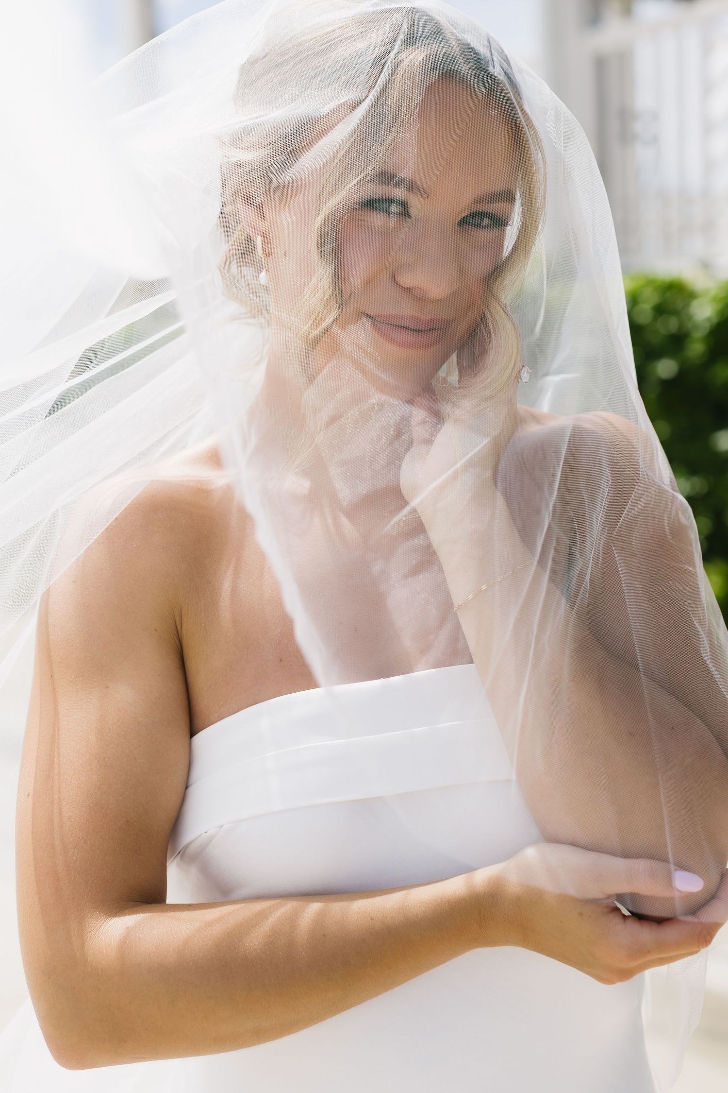 Closeup sequence showing a bride in a white dress adjusting her delicate veil in natural light.