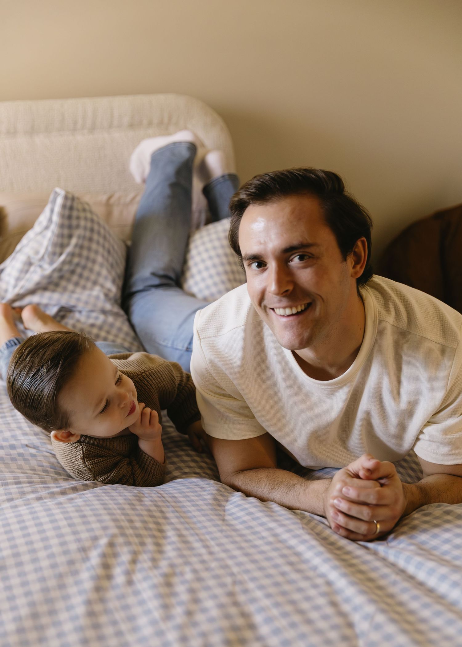 Intimate moments captured of family members lying together on a bed in casual white clothing.