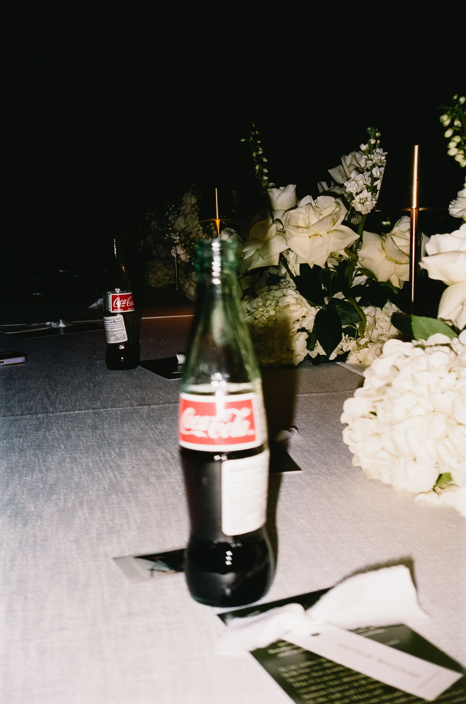 Glass bottles and white floral arrangements on a dark table at a wedding reception.