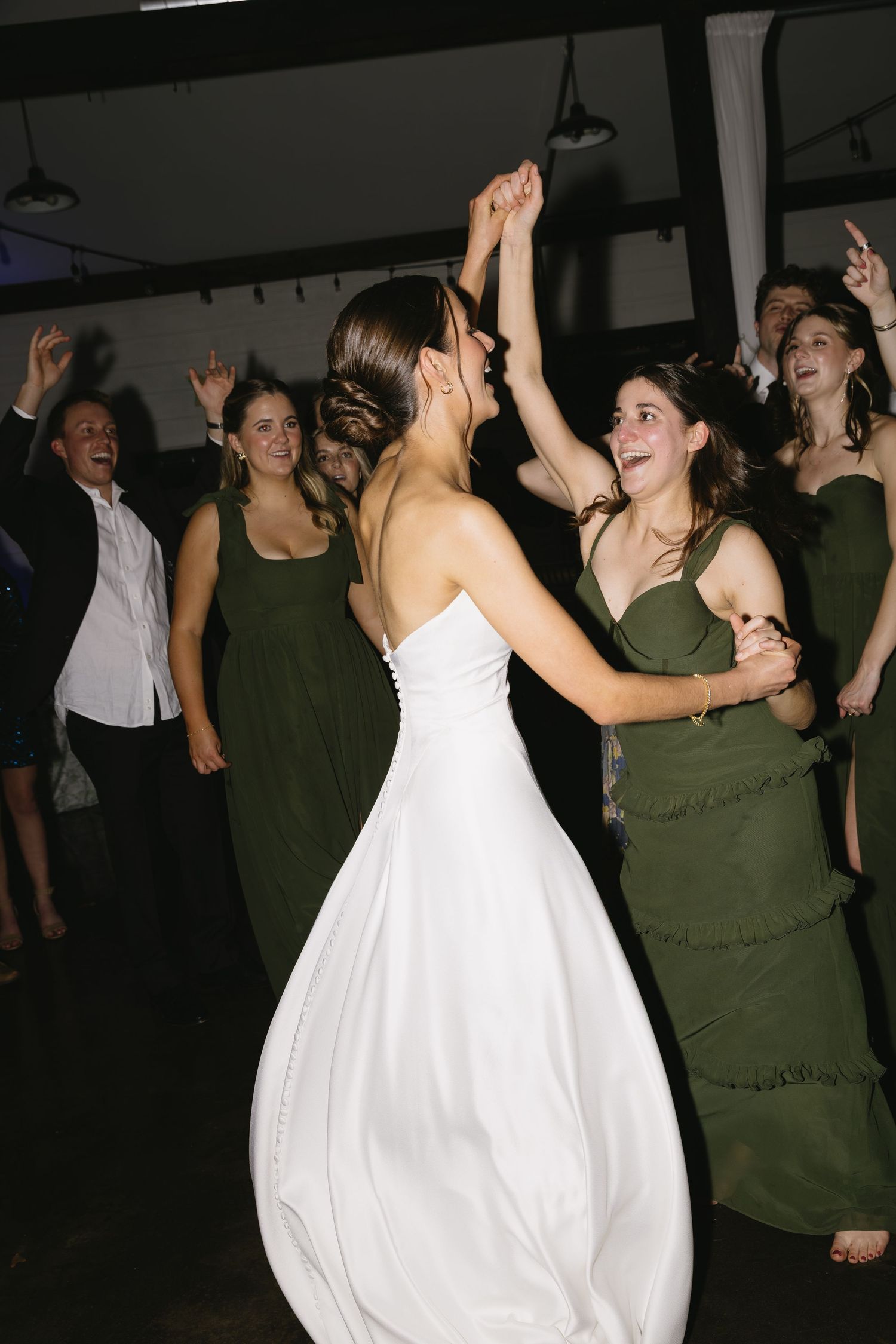 Wedding reception dance floor filled with joyful guests celebrating in a dimly lit venue.