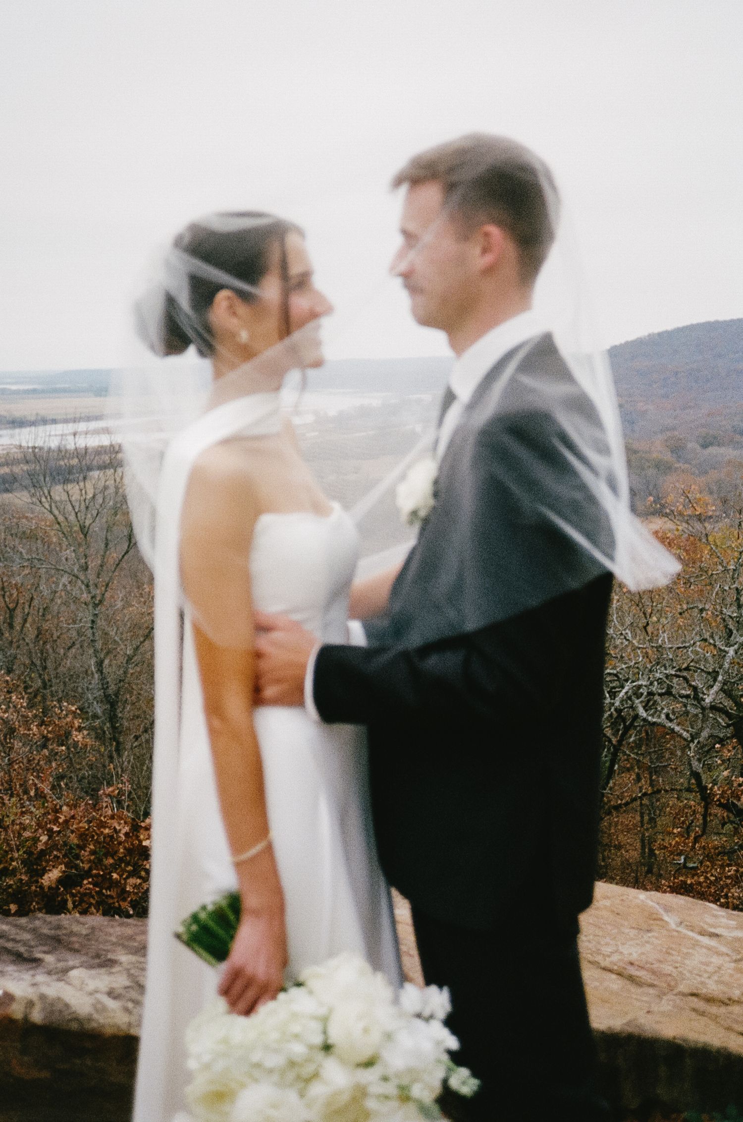 A romantic wedding couple embraces on a mountaintop overlooking an autumn landscape.
