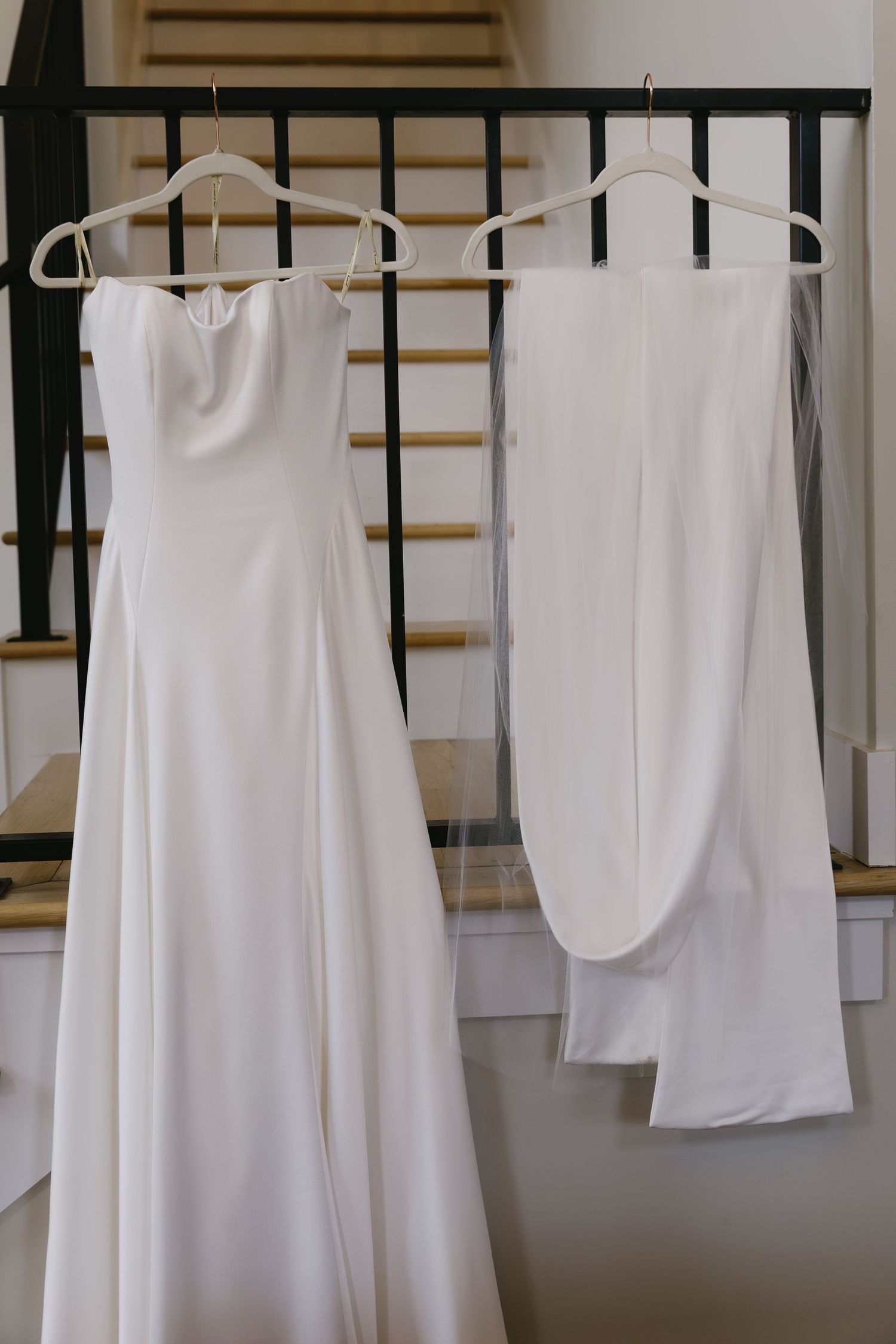 Row of white wedding dresses and garments hanging on black clothing rack.