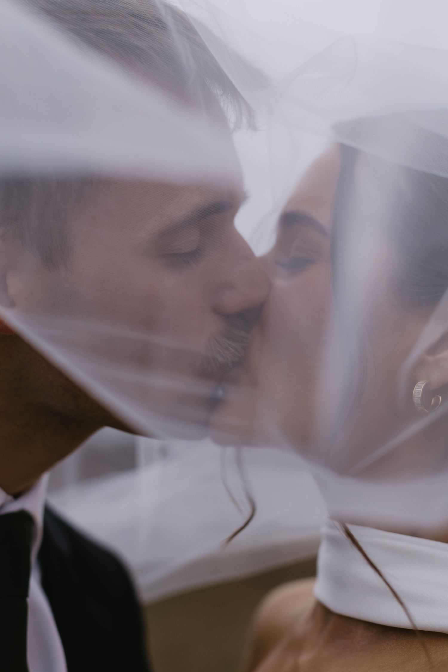 Romantic wedding couple sharing an intimate moment behind a sheer veil against a soft light background.