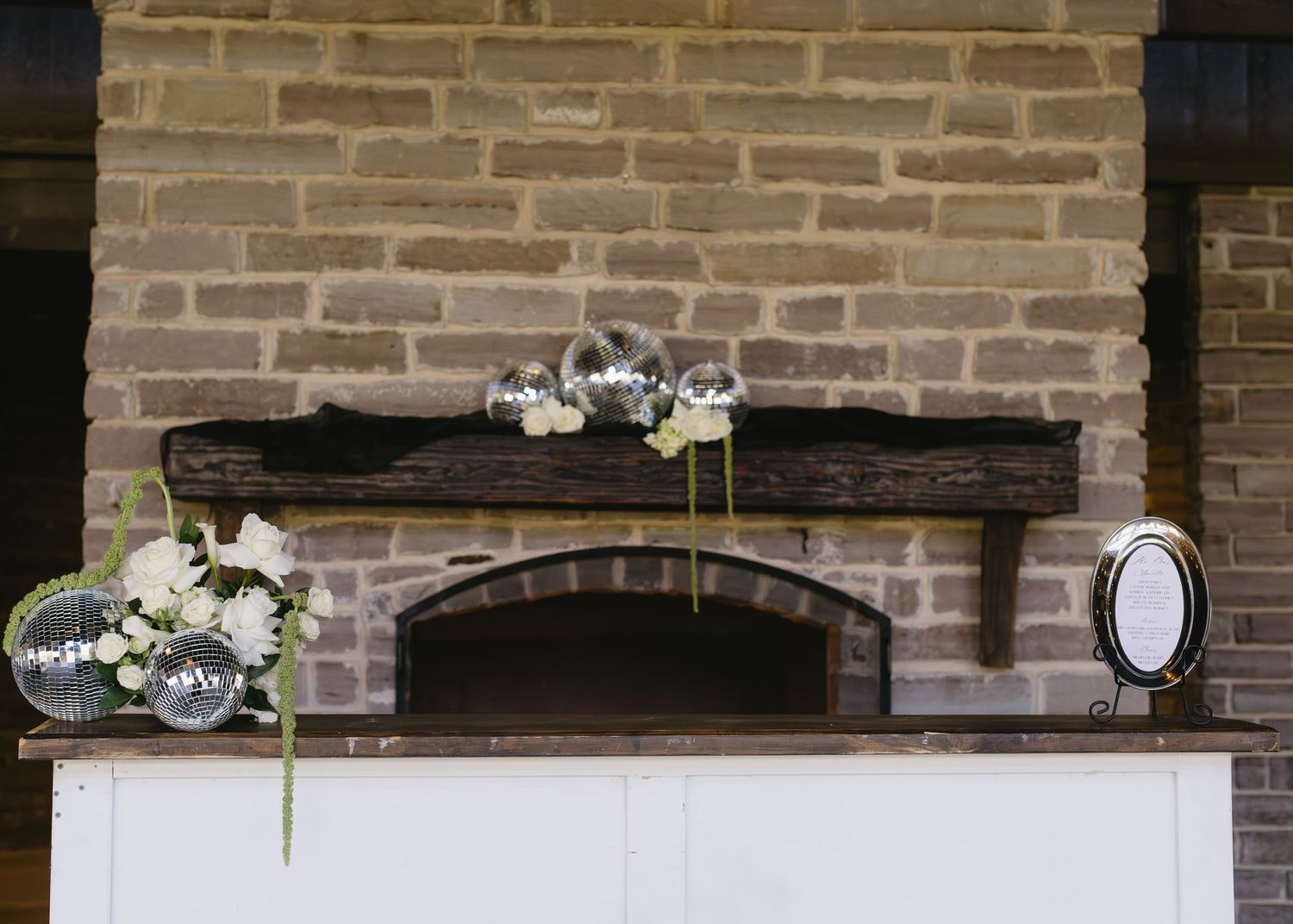 Rustic brick wall decorated with floral arrangements and string lights for wedding reception.