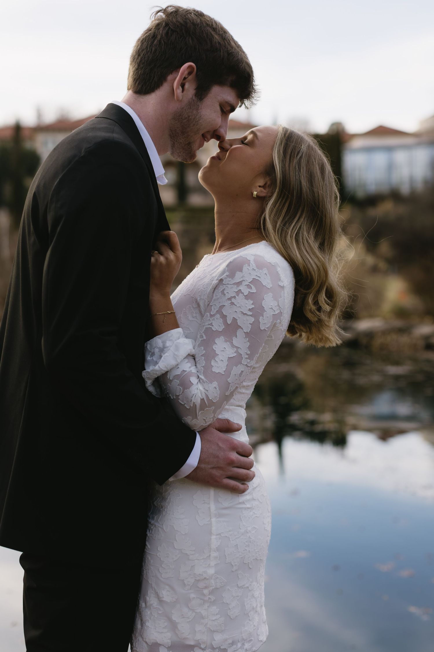 An intimate moment between newlyweds by a reflective pond during their wedding photoshoot.