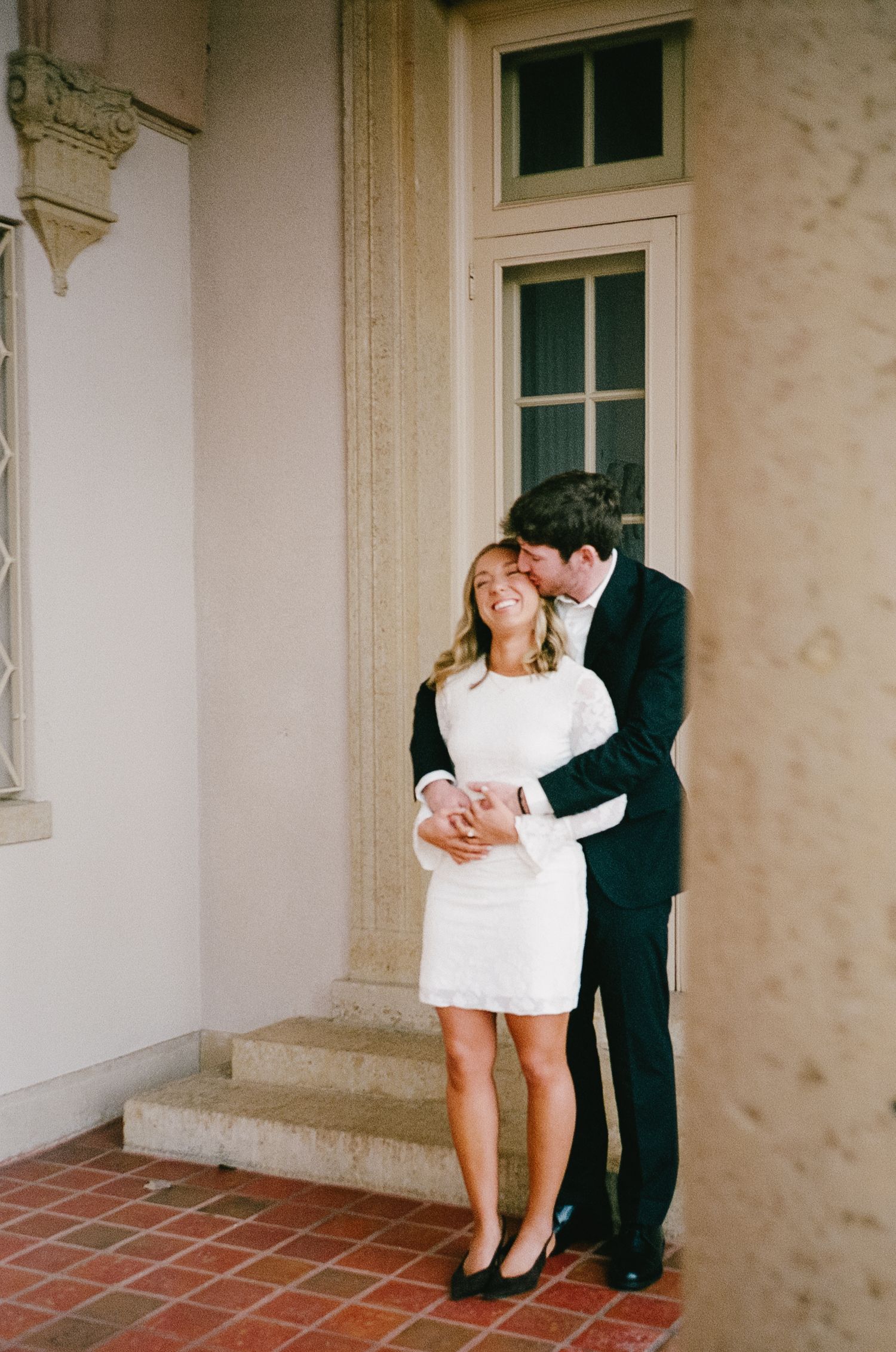 A romantic couple embraces in a series of tender moments against a light colored building wall.